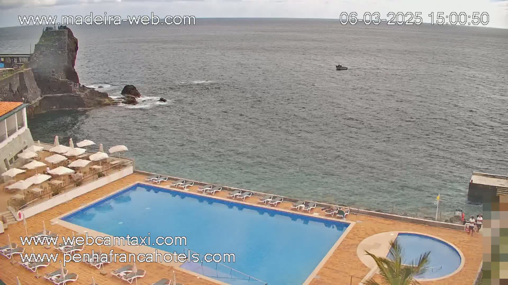 An outdoor swimming pool and patio area are situated next to the ocean on an overcast day.