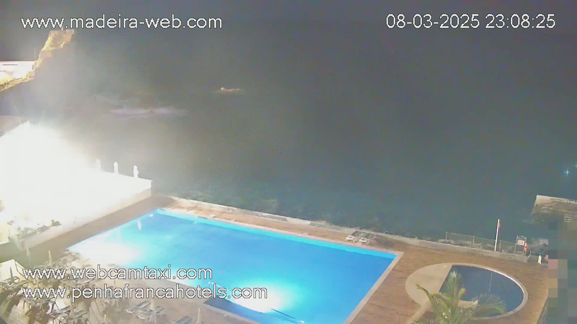 An outdoor nighttime scene shows a rectangular swimming pool next to the ocean under a dark, hazy sky.