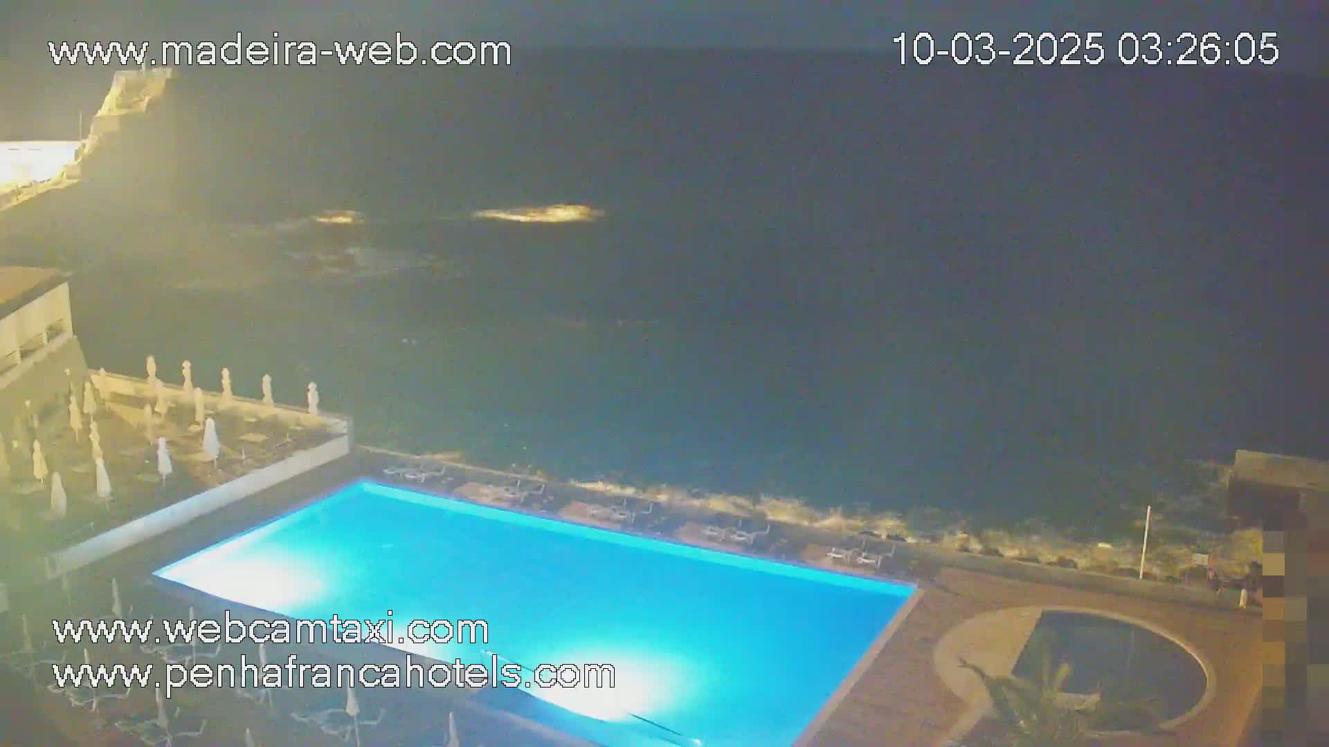 An illuminated swimming pool and surrounding patio area overlook a dark ocean at night.