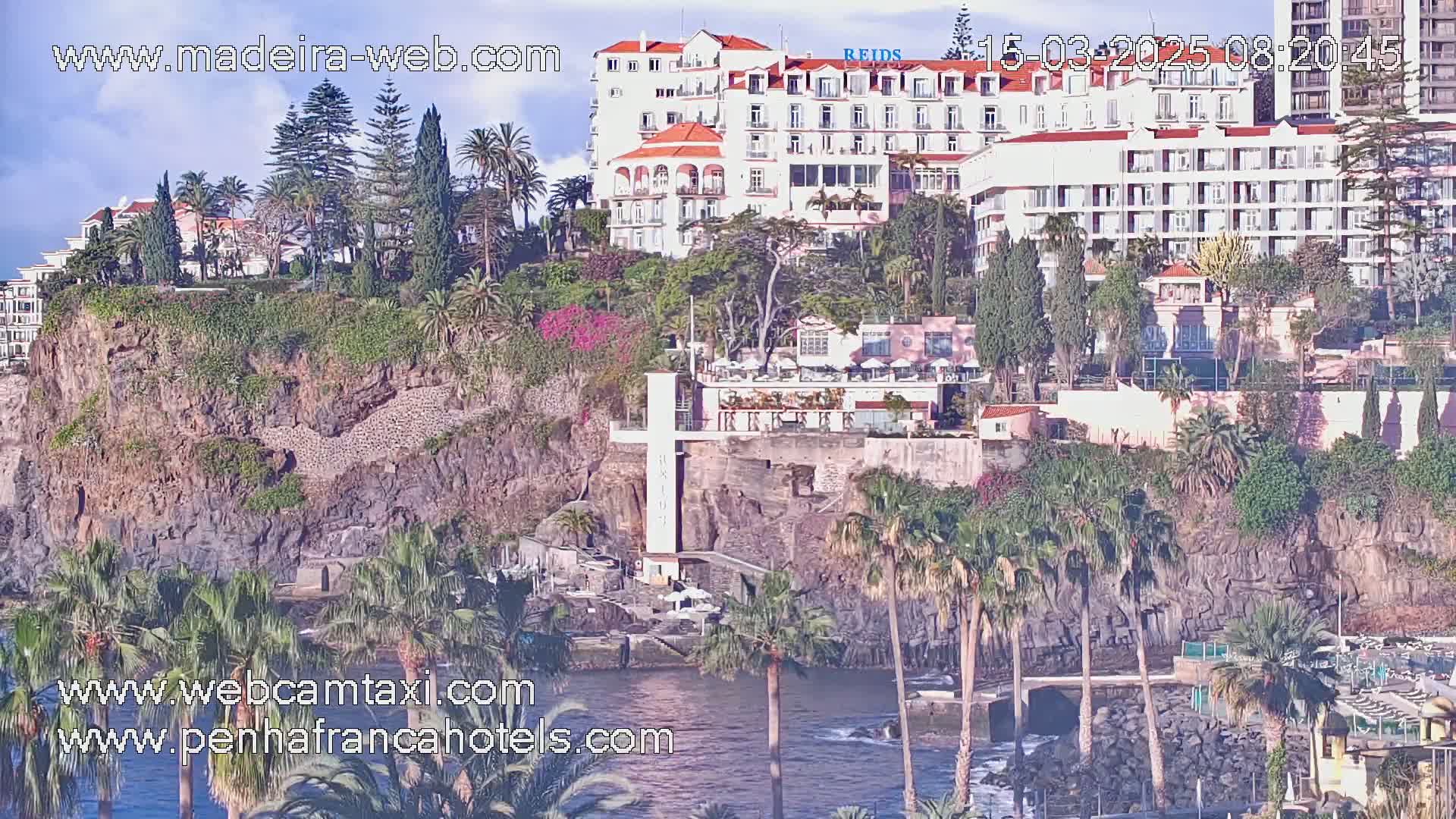 A cliffside resort with palm trees and ocean views on a partly cloudy day.