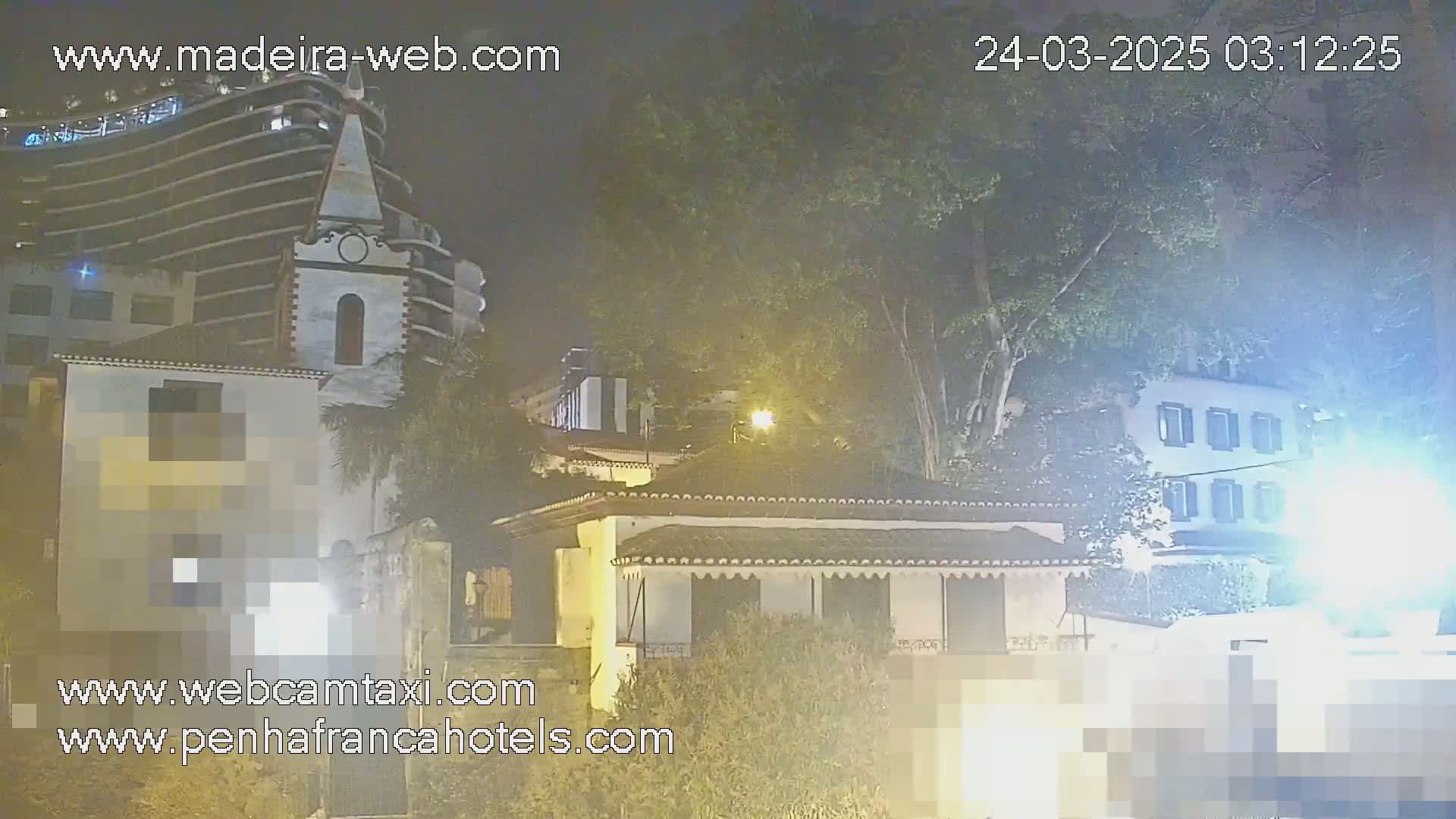 A nighttime view of buildings, including a church and a modern high-rise, partially obscured by trees and haze.