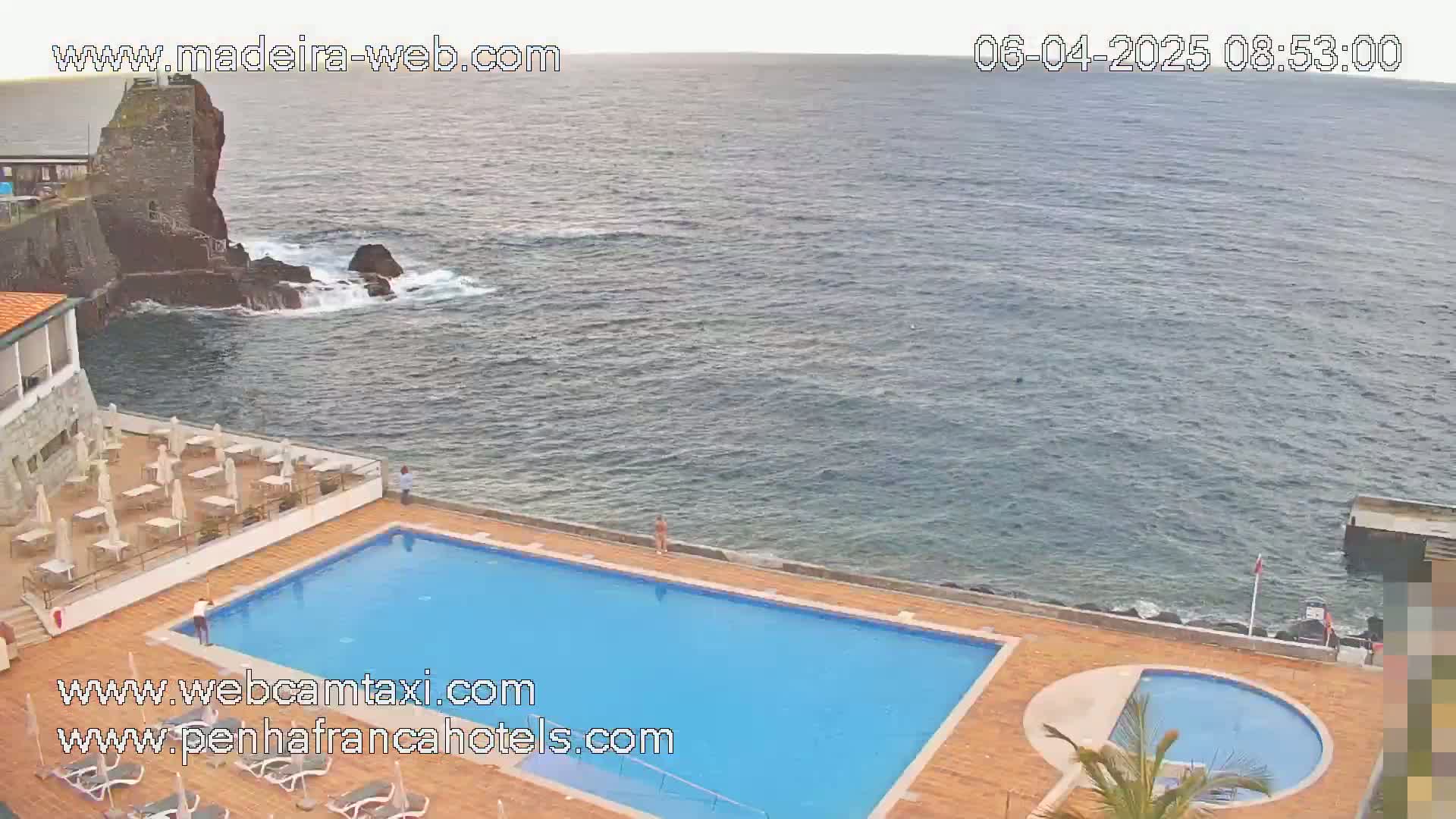 An outdoor pool and patio area next to the ocean on an overcast day.