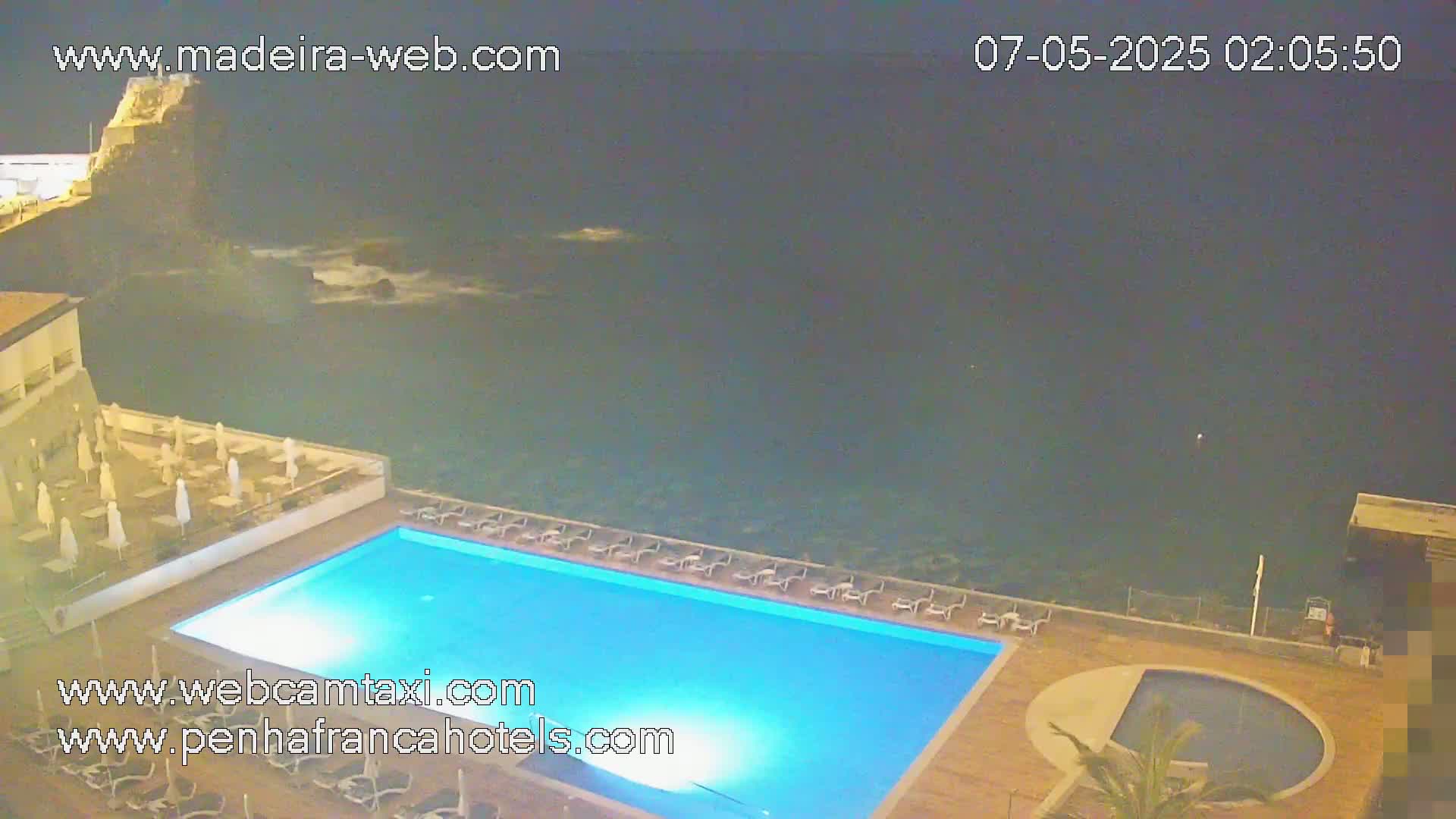 A nighttime view of a resort pool area overlooking a dark ocean with some small waves.