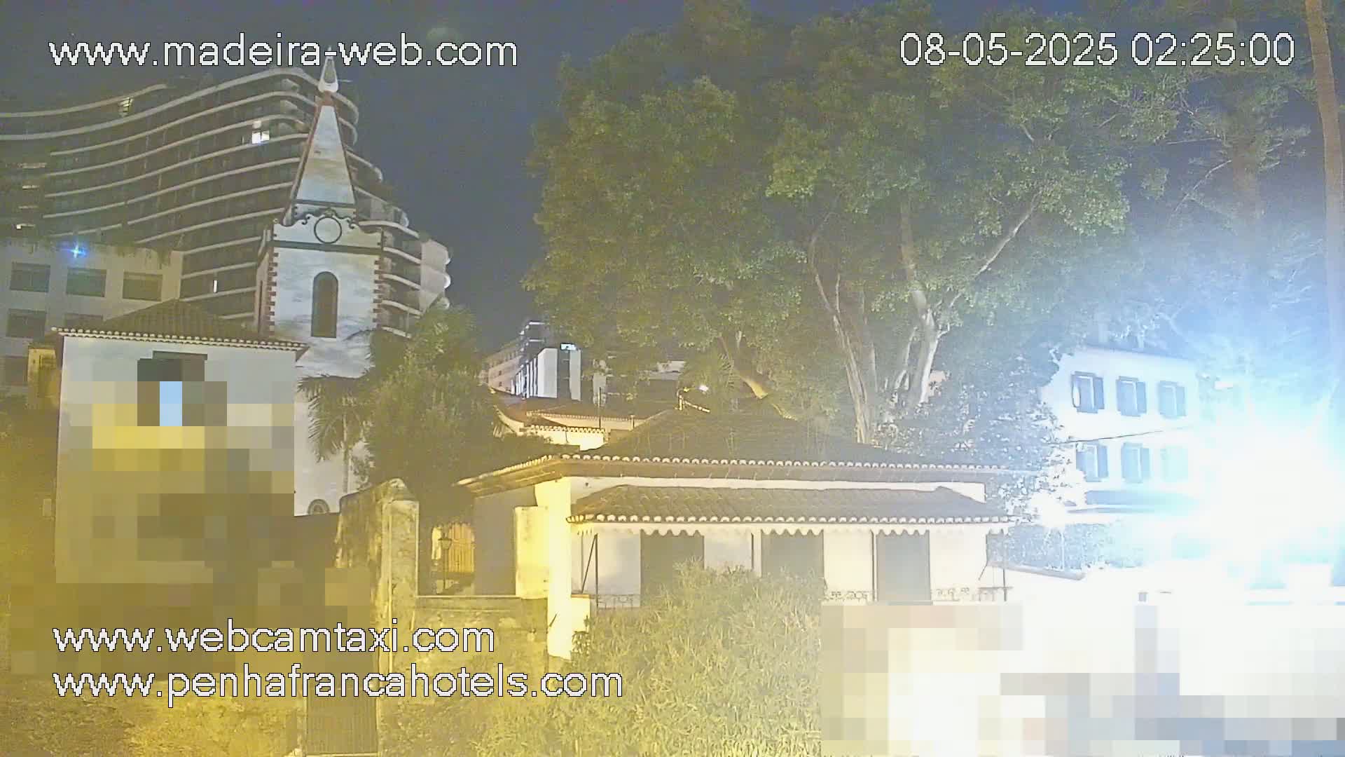 A nighttime view of buildings, including a church and a multi-story hotel, partially obscured by trees and hazy light.
