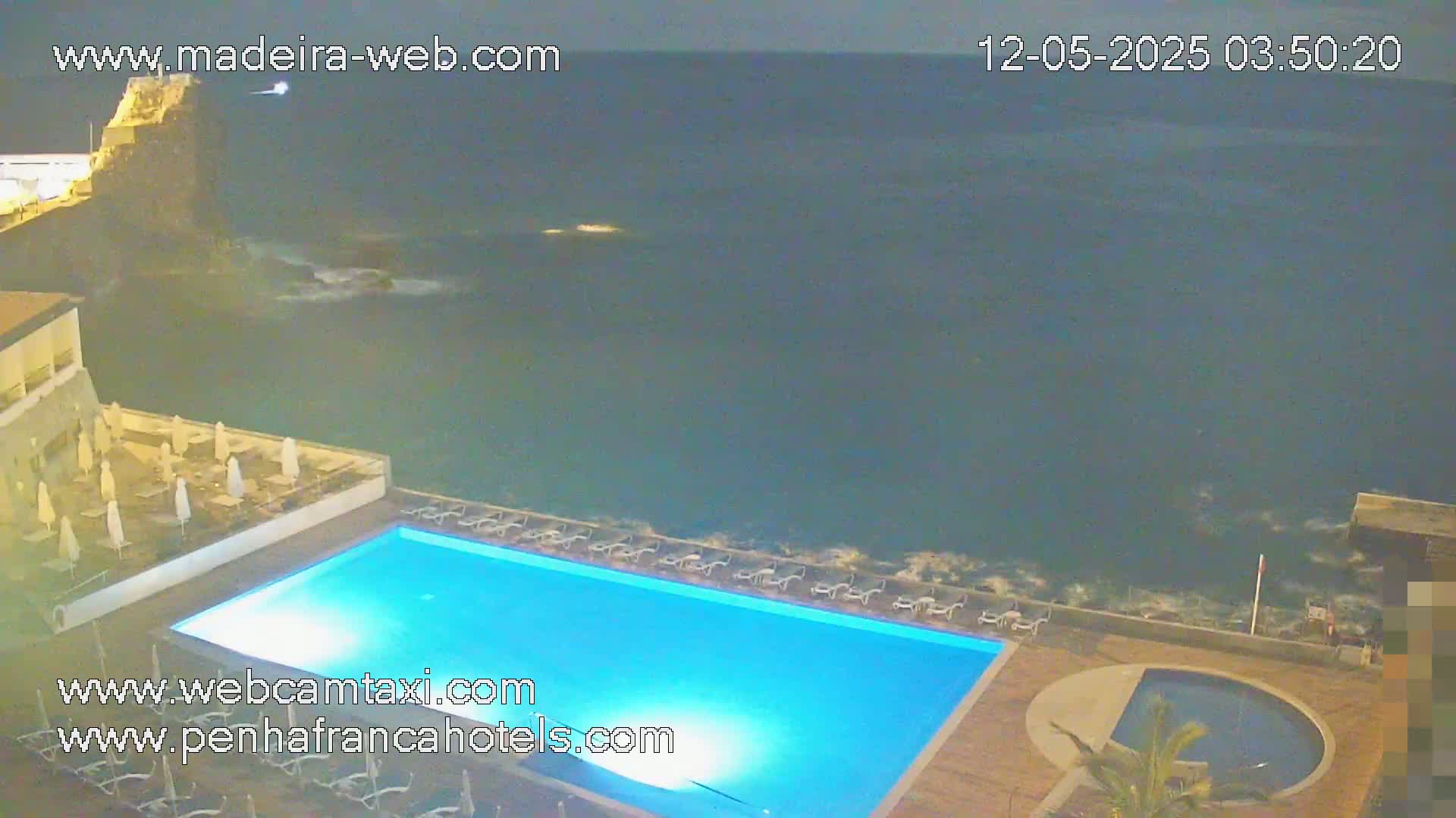 A nighttime view of a resort pool area overlooking a dark, wavy ocean.