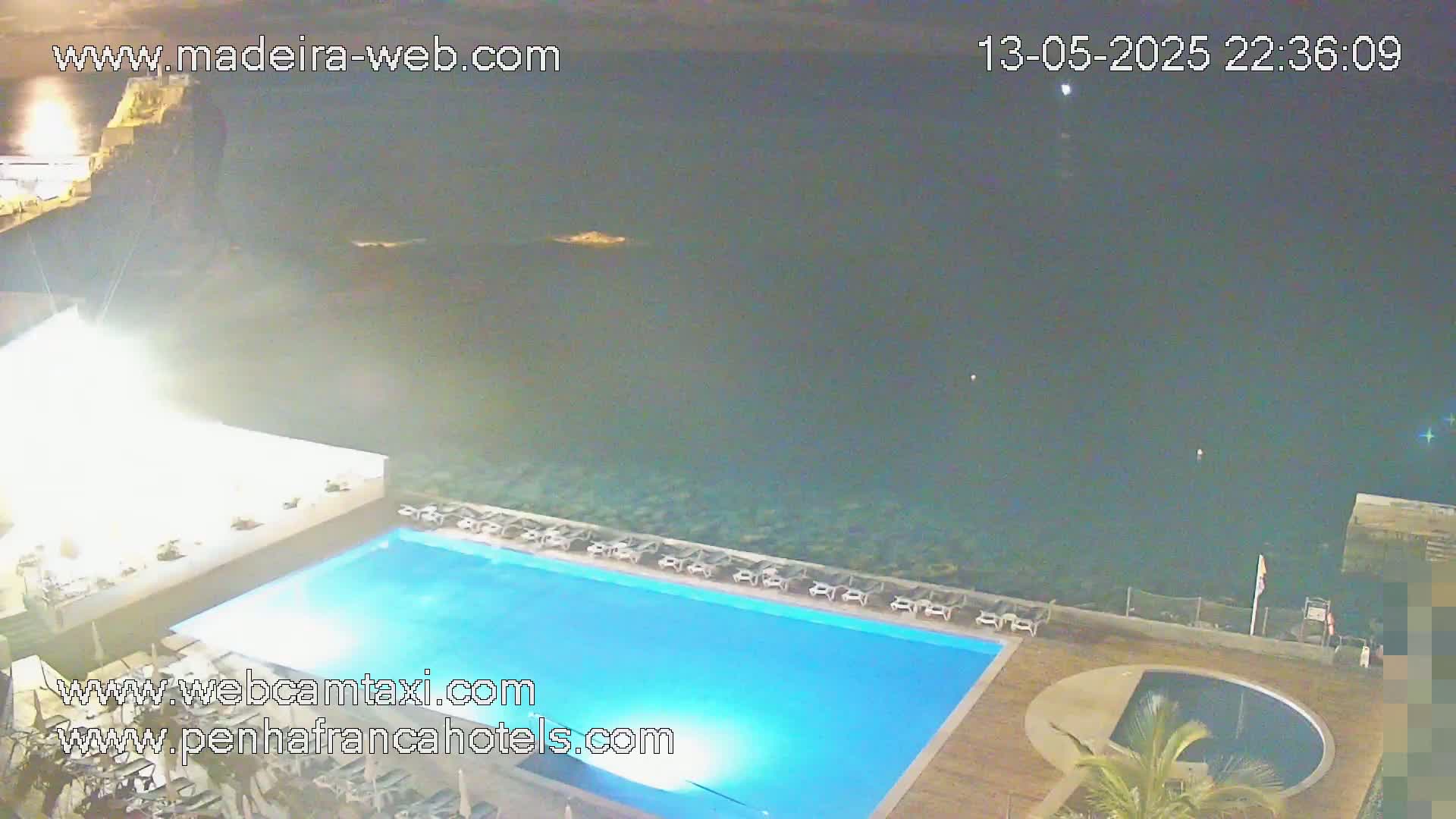A nighttime view of a rectangular swimming pool and a smaller circular pool at a resort overlooking a dark ocean.
