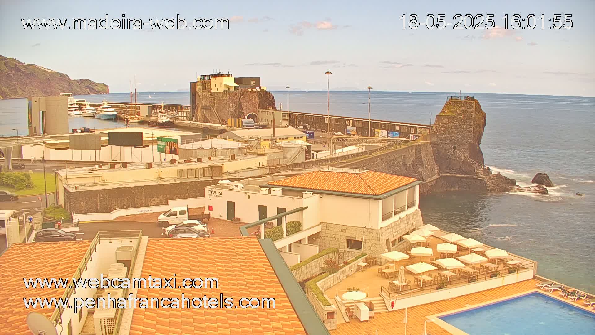 A seaside resort town with a harbor, featuring boats, buildings, a pool, and a partly cloudy sky.