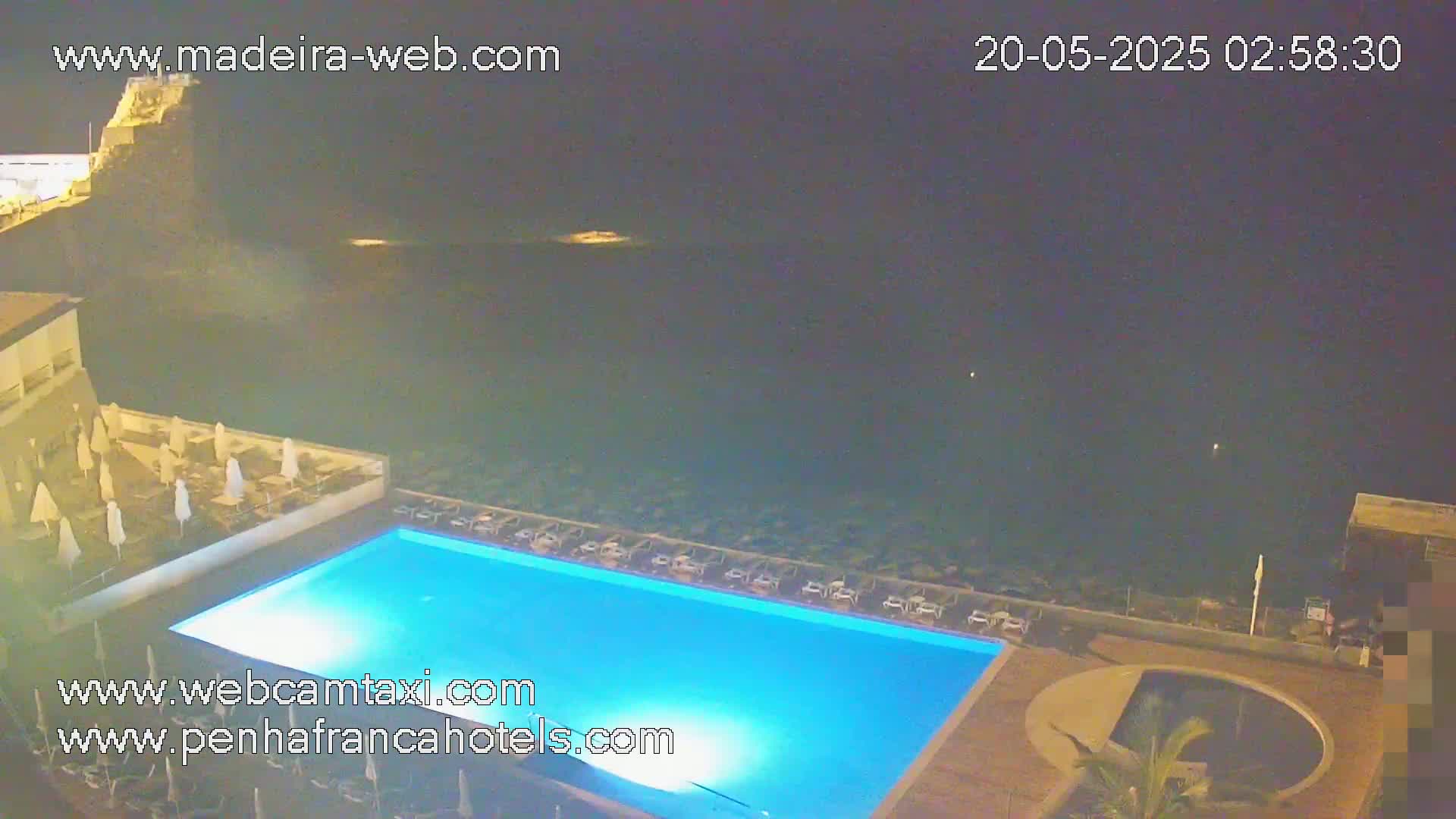 An illuminated swimming pool and surrounding patio area overlook a dark ocean at night.