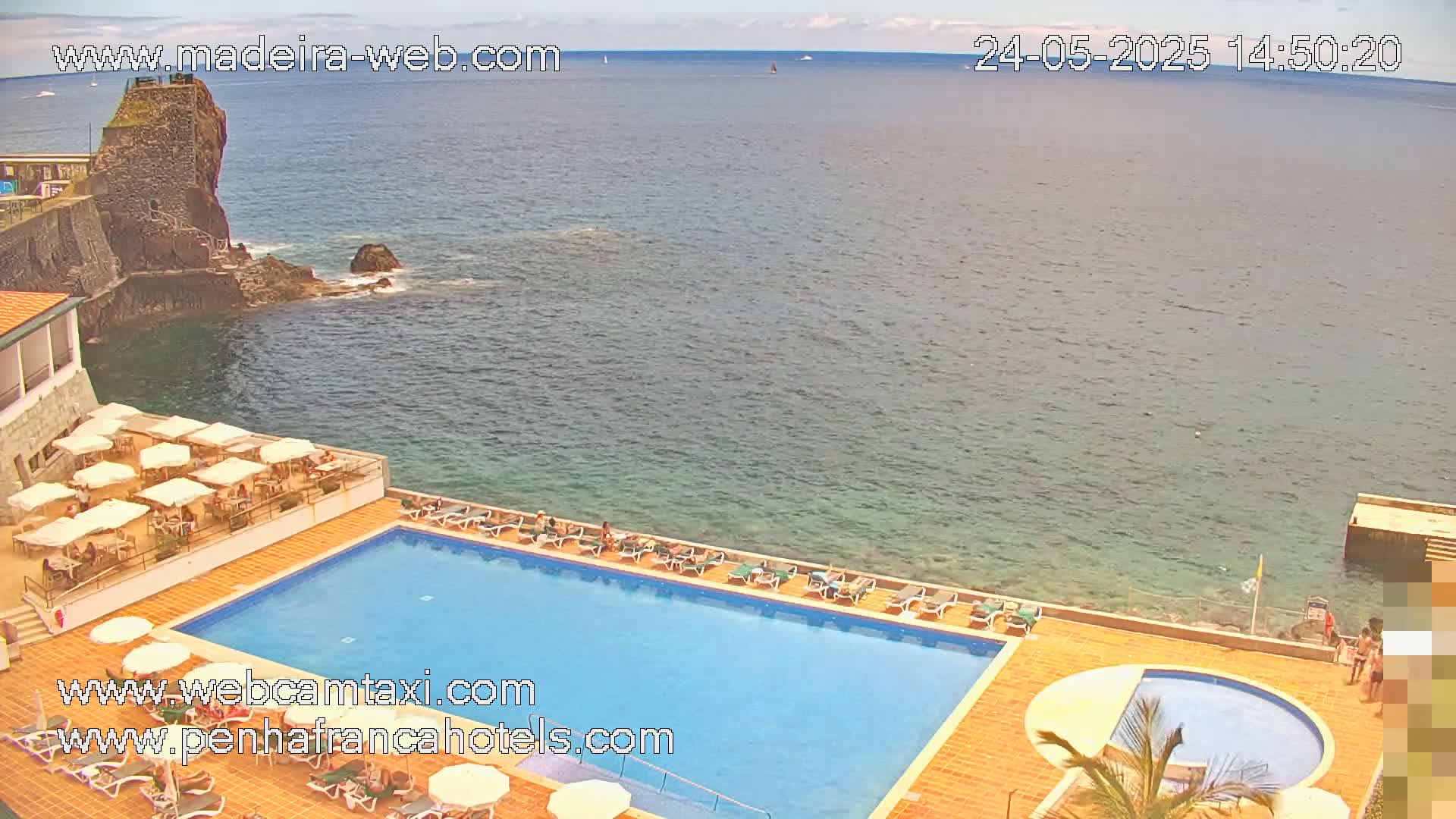 An outdoor swimming pool at a hotel overlooks a calm ocean on a partly sunny day.