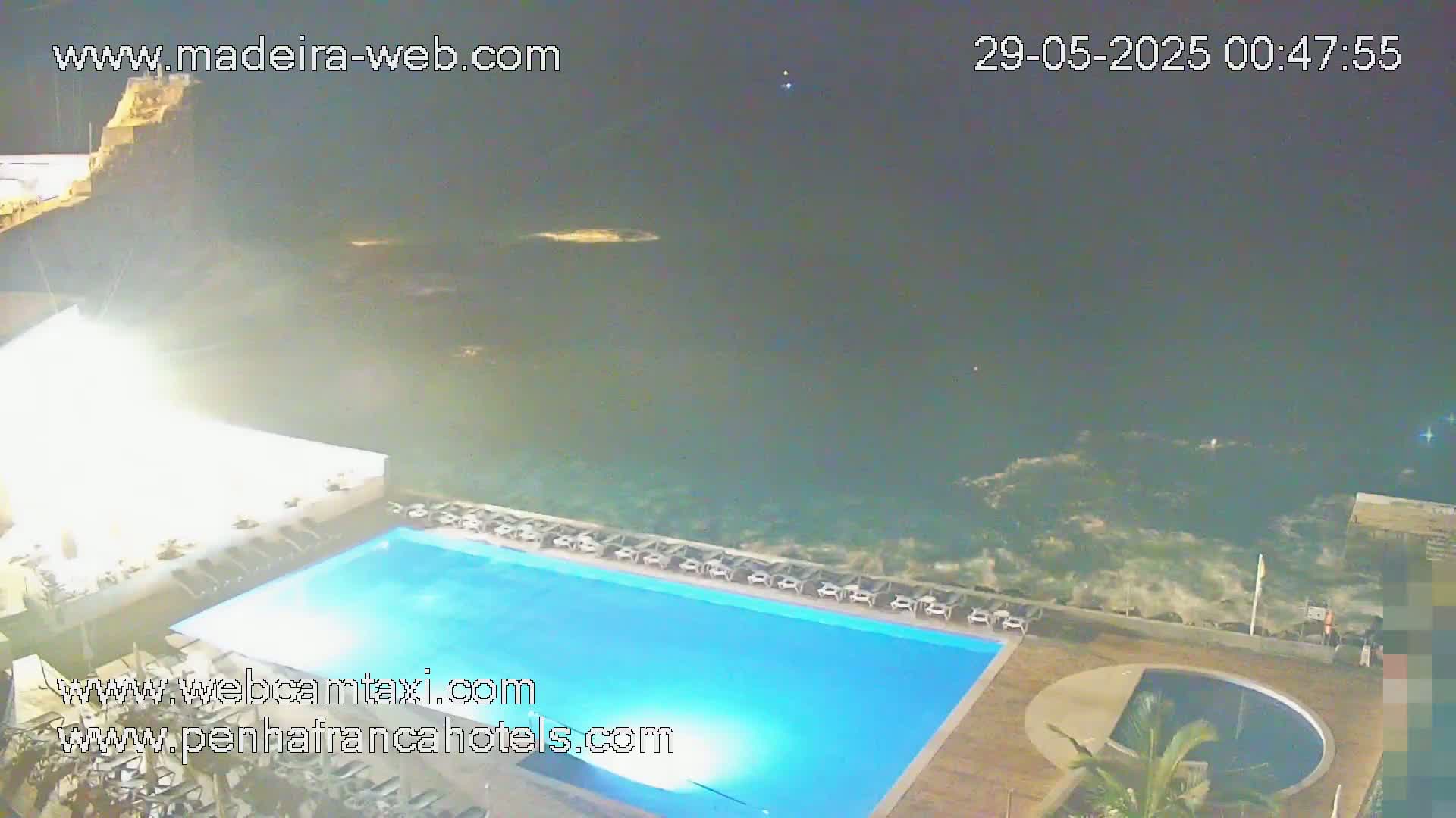 A nighttime view of a resort pool area overlooking a dark ocean with moderate waves.