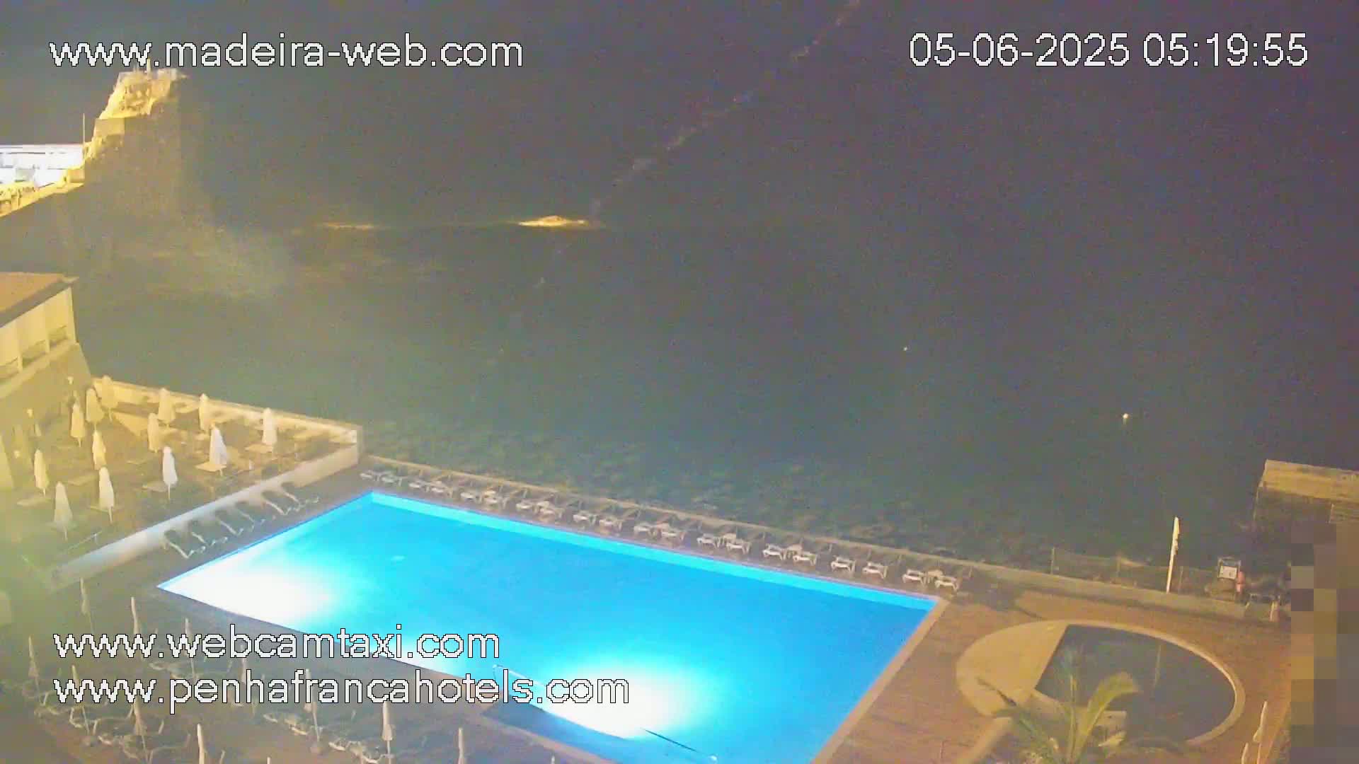An illuminated rectangular swimming pool is situated at night next to a dark ocean, under a clear, dark sky.