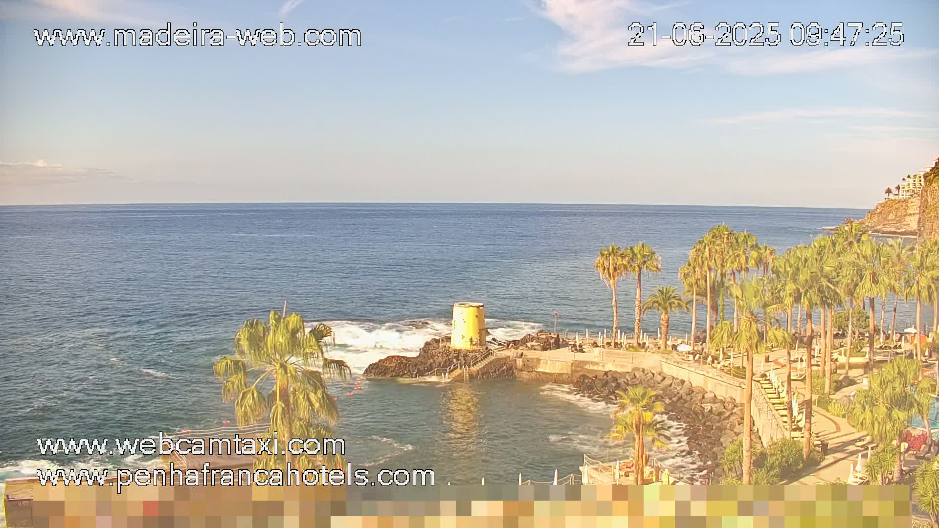 A tranquil ocean scene with palm trees lining a rocky shoreline under a partly sunny sky.
