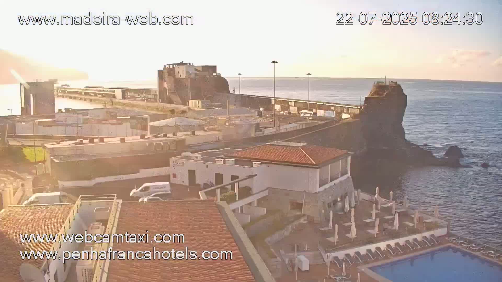A coastal town scene at sunrise, showing buildings, a harbor, and calm ocean water.