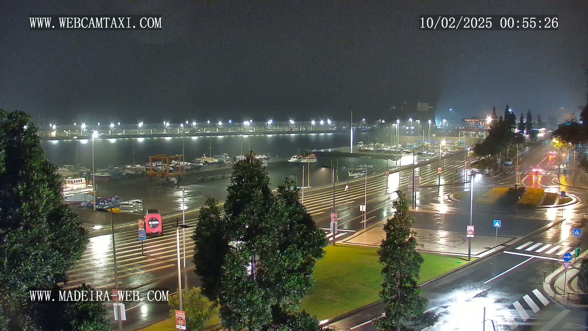 A nighttime, rain-slicked marina scene shows a bridge, boats, and roadways illuminated by streetlights.