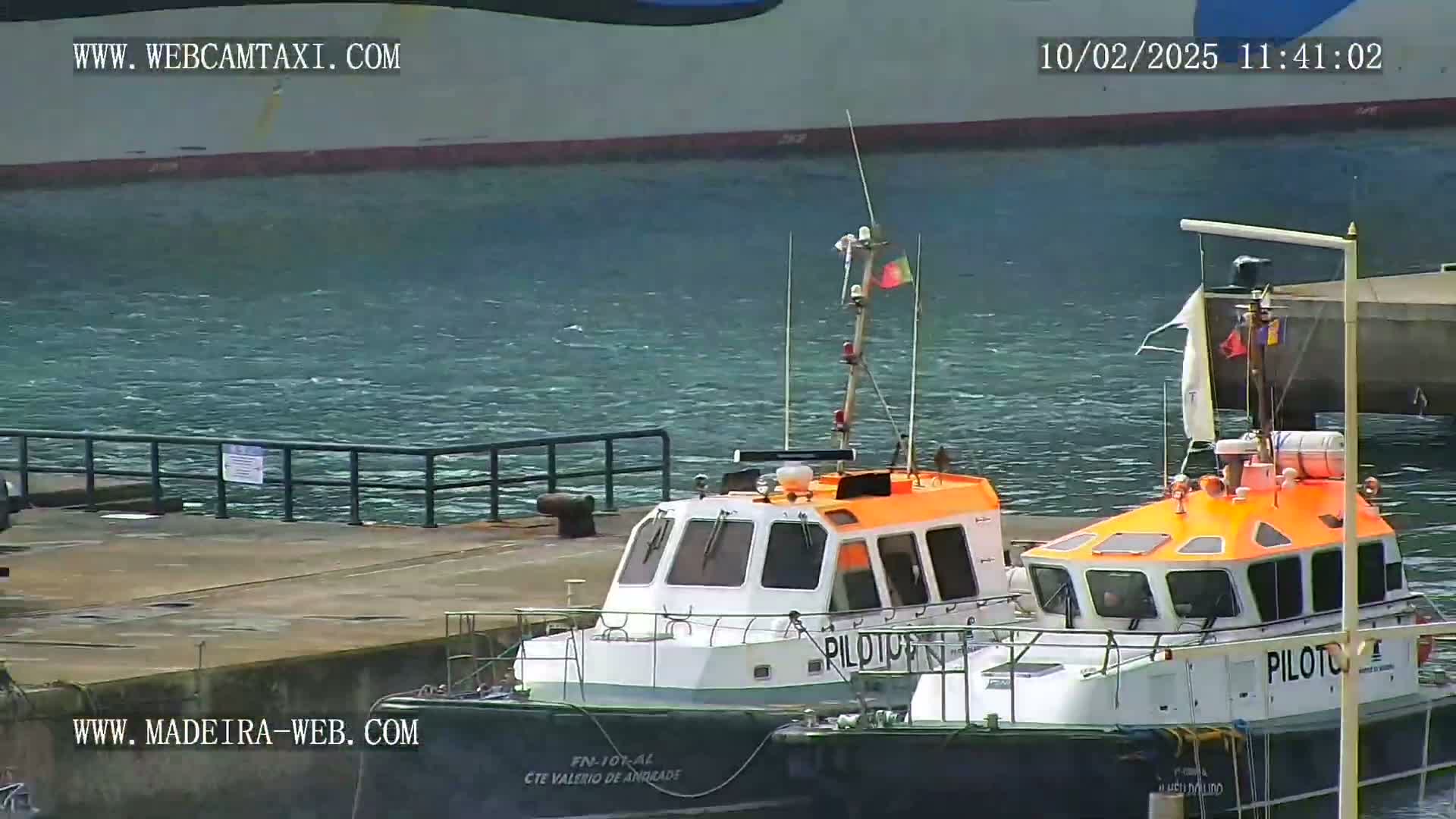 Two orange and white pilot boats are docked near a larger ship in choppy water.