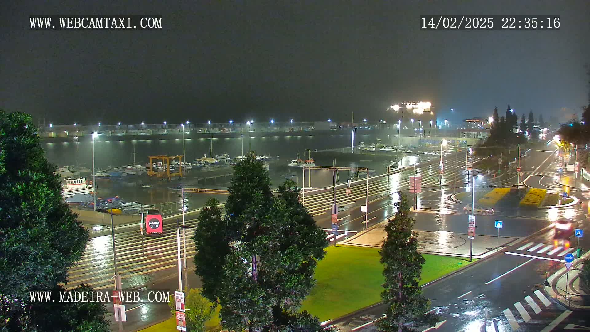 A marina and surrounding roadways are shown at night in the rain, with lights illuminating the wet surfaces.