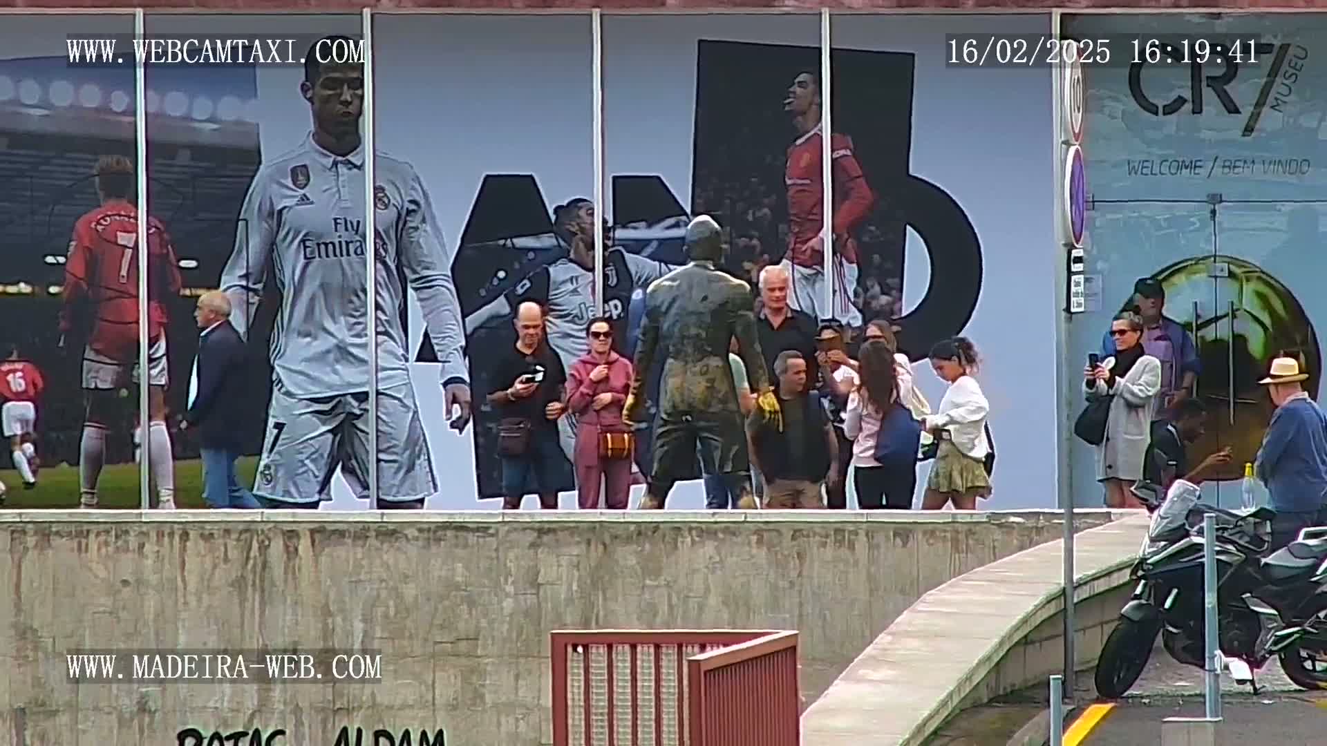 A large outdoor mural depicting Cristiano Ronaldo stands behind a group of people taking photos, some of whom are on motorcycles.