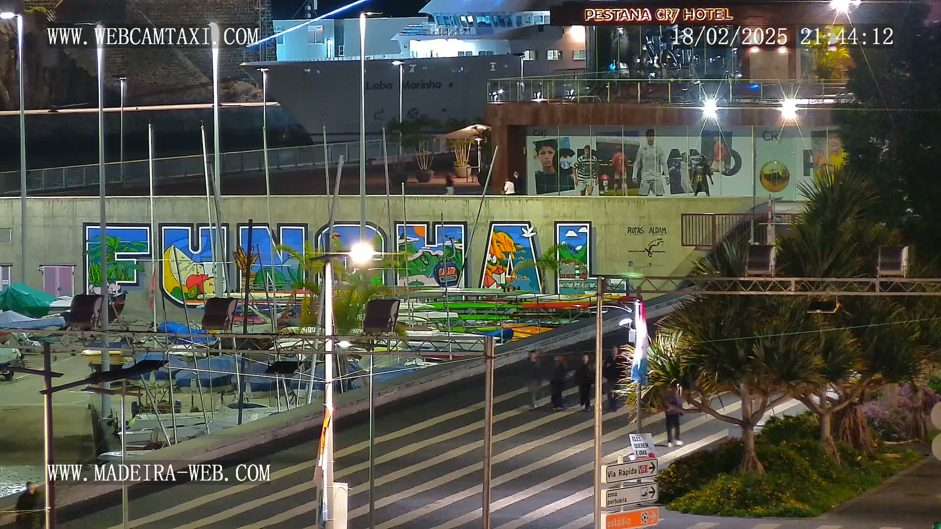 A nighttime harbor scene shows a large mural of "Funchal" on a wall beside a marina filled with boats under bright lights.