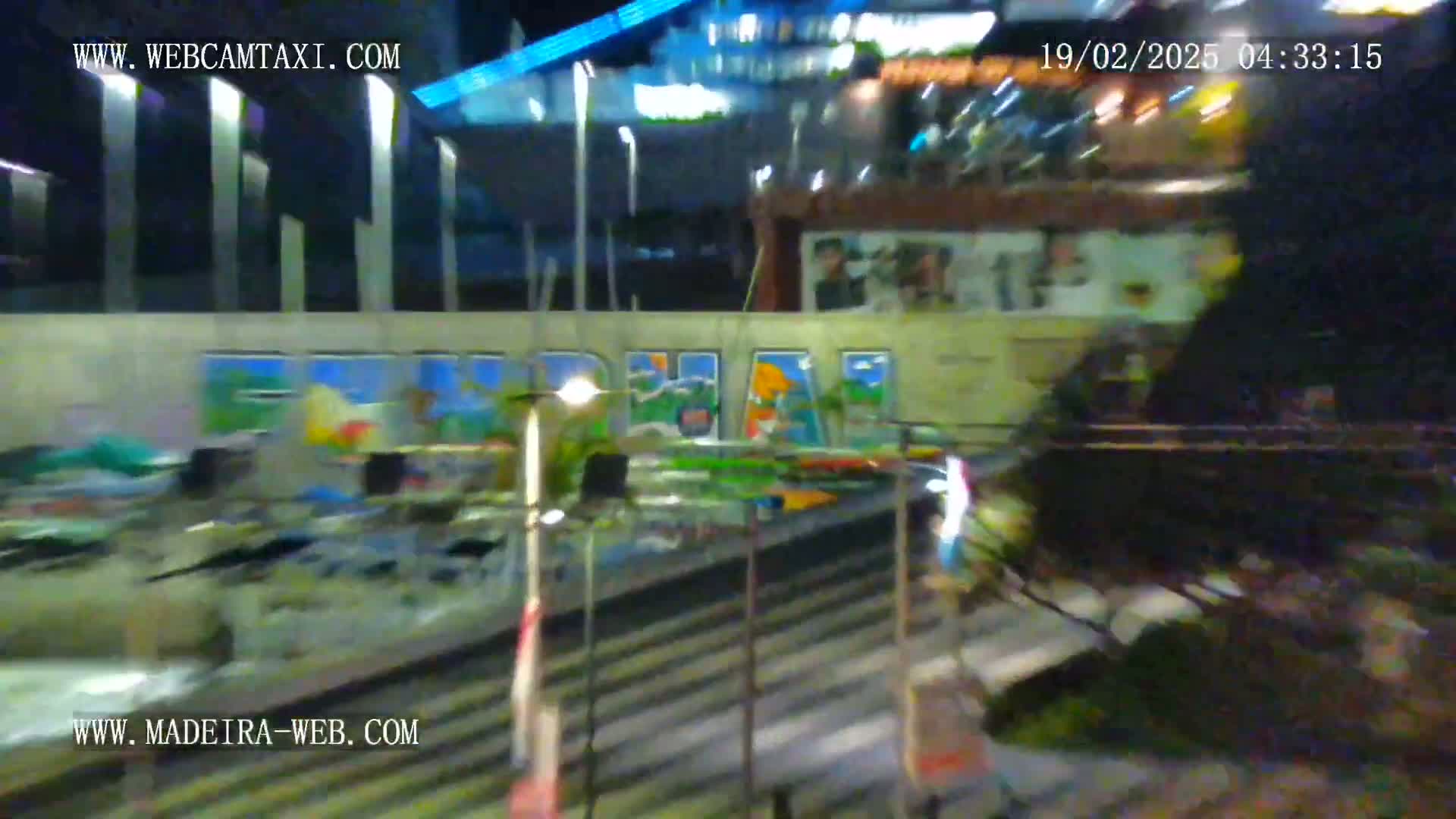 A nighttime, blurry view of a wall with painted scenery and what appears to be a fairground ride or similar attraction.