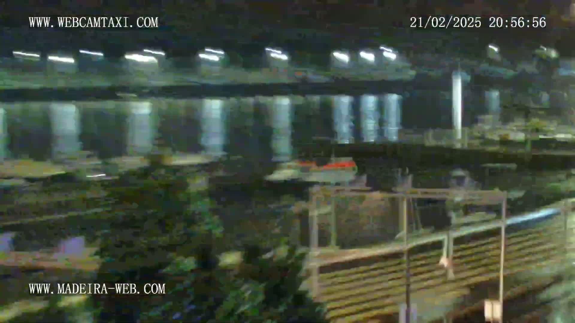 A nighttime, blurry view of what appears to be a transportation hub or industrial area with various structures and vehicles, possibly a train, under artificial lighting.
