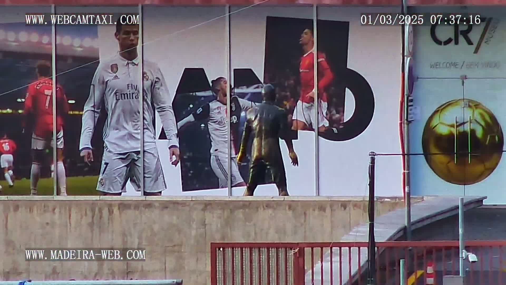 A large outdoor billboard displays images of Cristiano Ronaldo in various soccer uniforms, along with a statue-like figure, and a large golden soccer ball.