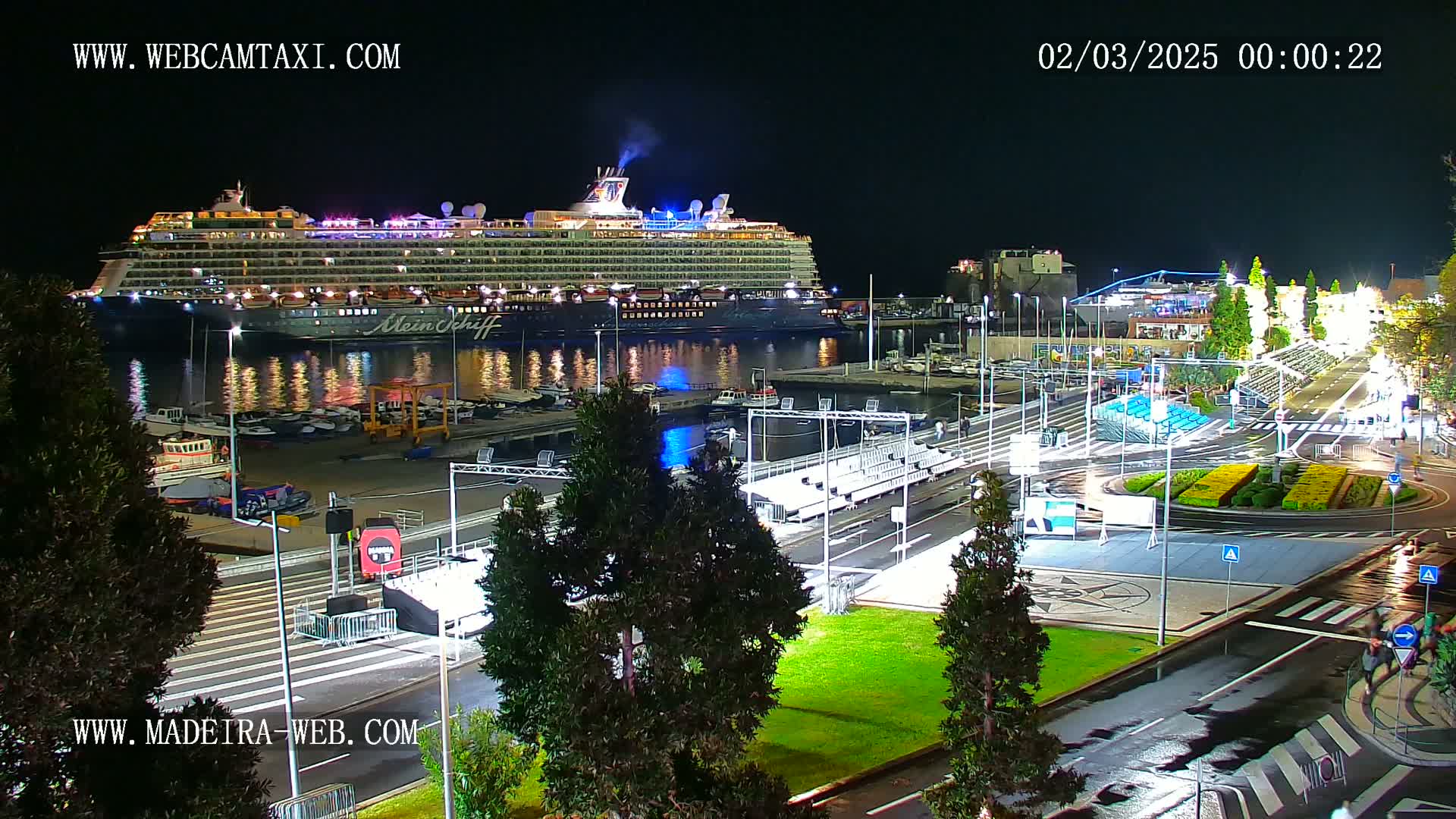A large cruise ship is docked at a port at night, under slightly wet conditions.