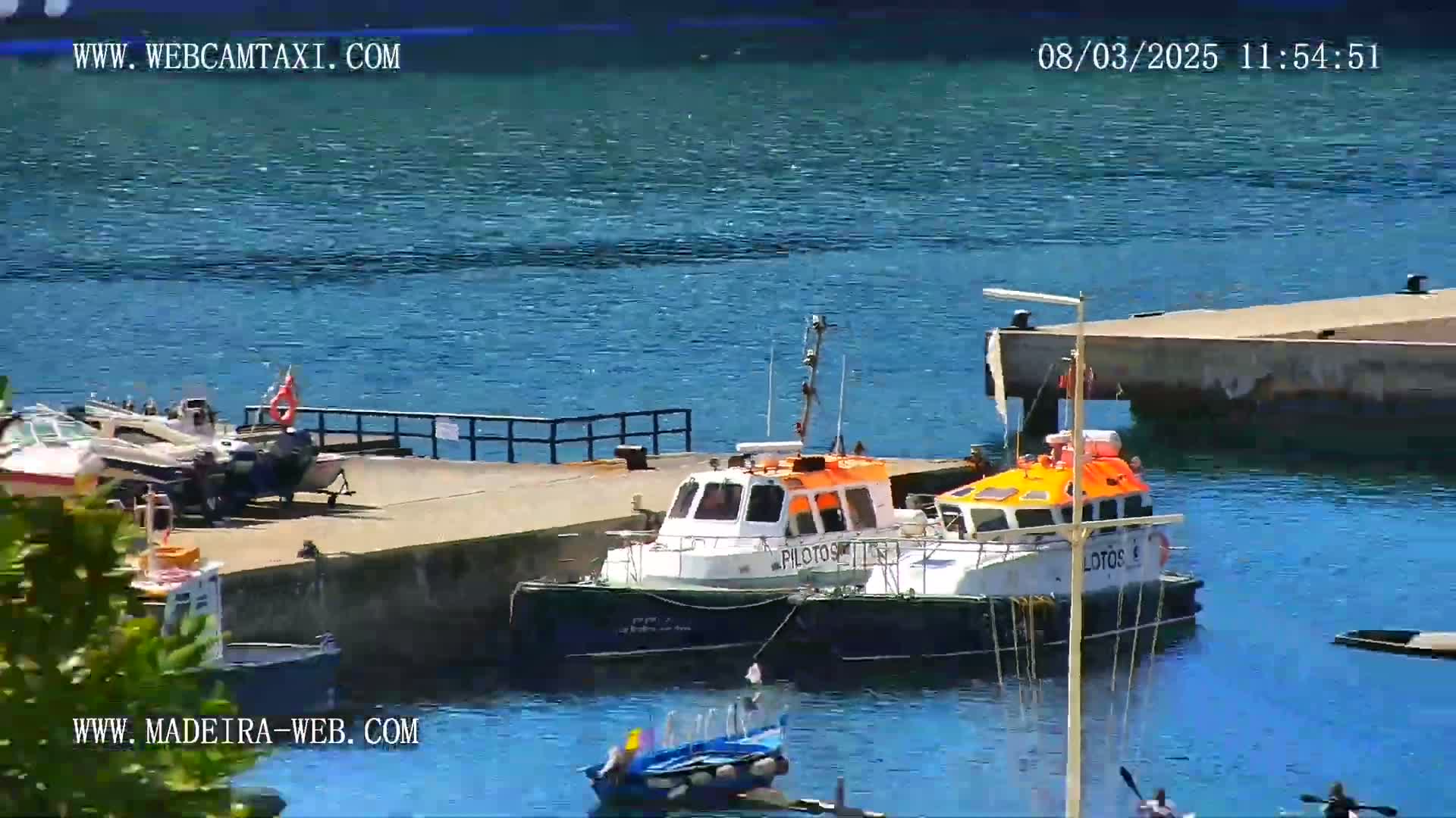 Two pilot boats are moored at a dock next to several other smaller boats, all on a sunny day with calm, blue water.