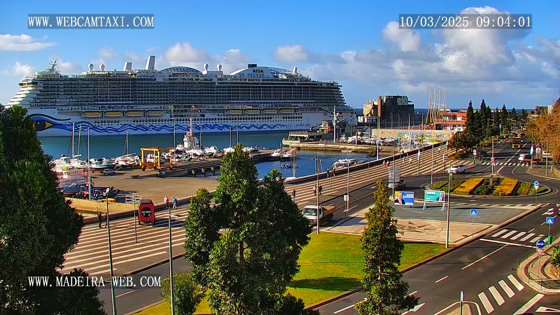 A large cruise ship is docked at a harbor on a sunny day with partly cloudy skies.