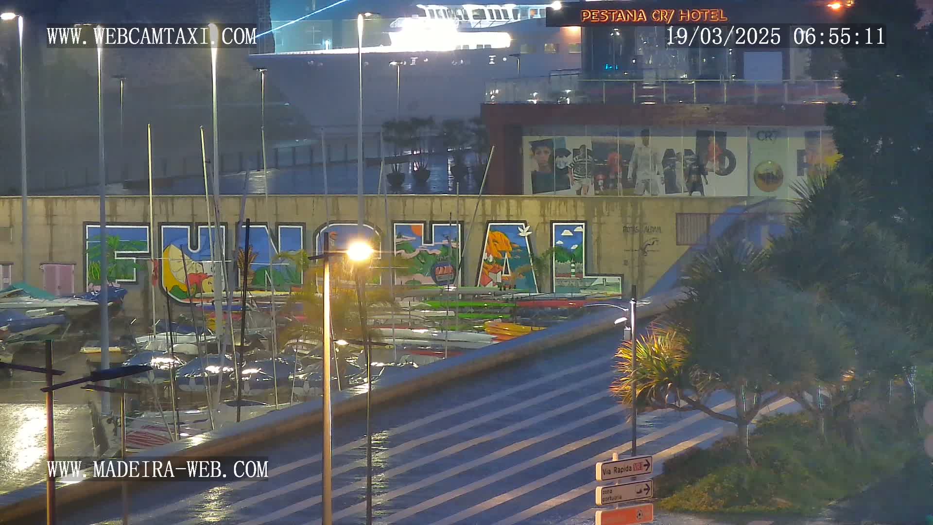 A rain-slicked marina at night features a large mural of the word "FUNCHAL," numerous boats, and a large cruise ship in the background.