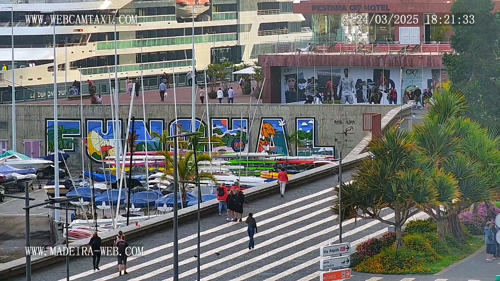 A harbor scene with numerous boats, a large cruise ship, and a mural reading "Funchal," is shown under sunny conditions.