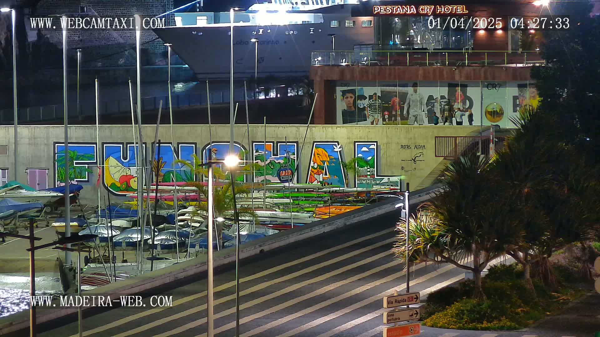 At night, a harbor scene shows a large mural of "Funchal" on a wall above numerous boats, a large ship, and palm trees under bright lights.