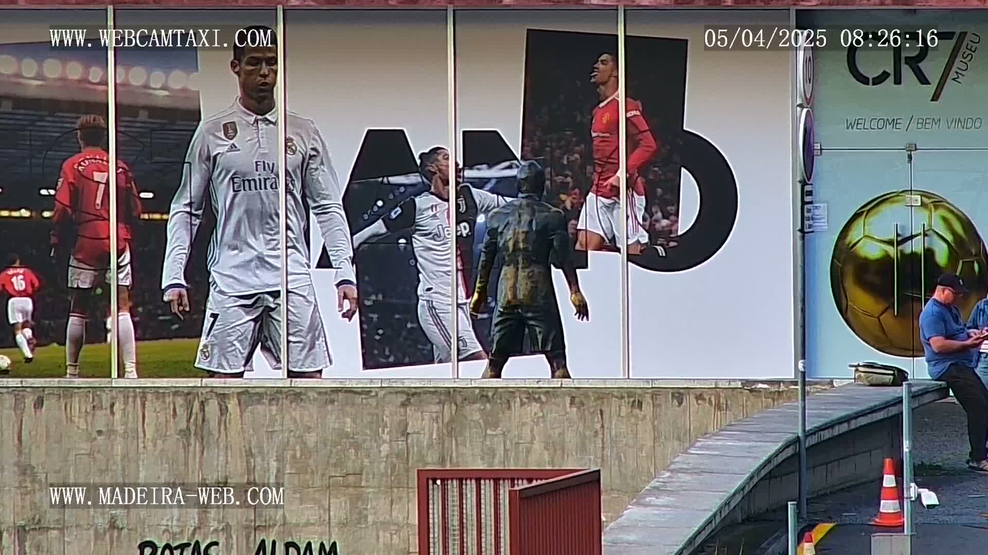 A large outdoor wall displays images of Cristiano Ronaldo in various soccer uniforms, along with a golden soccer ball and a statue of a man.