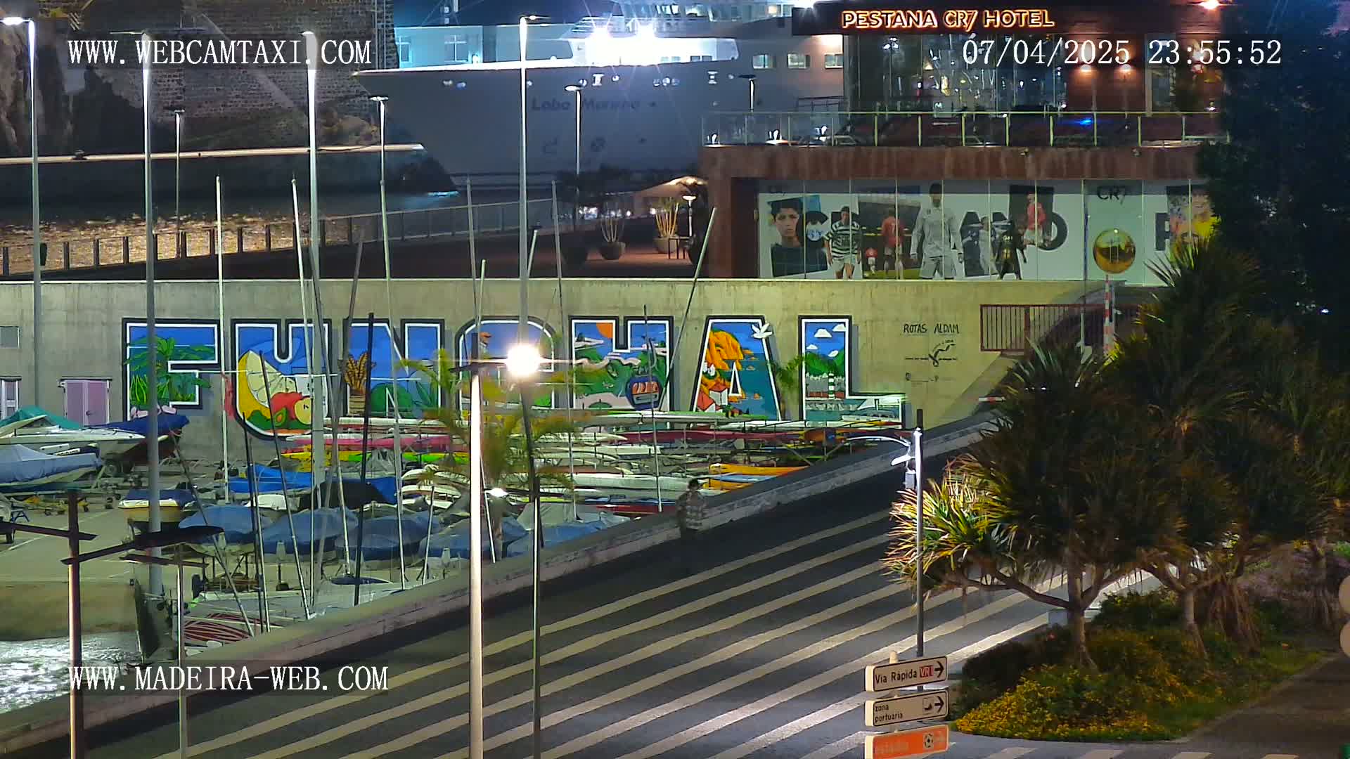 A nighttime harbor scene shows a large mural of "FUNCHAL" on a building, numerous boats docked, and palm trees illuminated by streetlights.