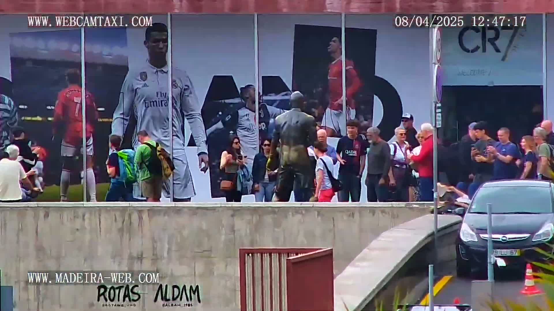 A group of people stand outside a building with large images of soccer players on the wall, under a partly cloudy sky.