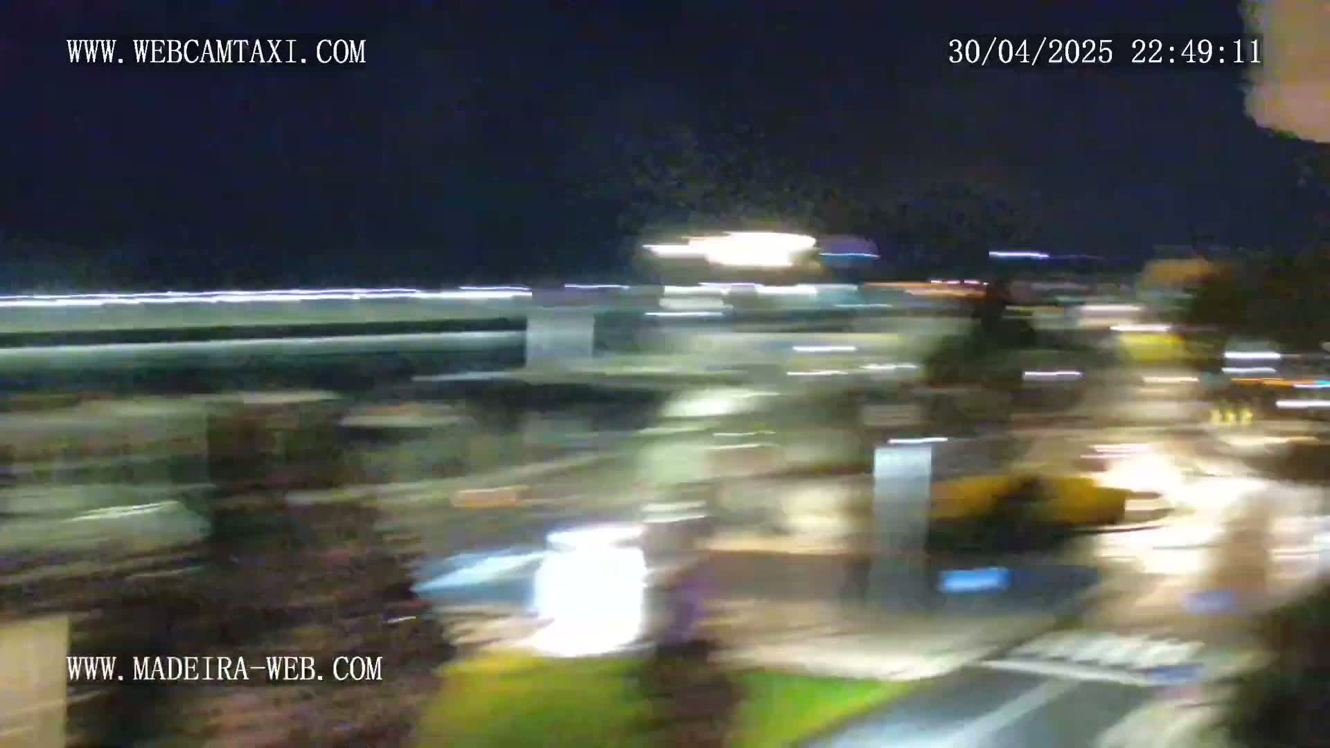 A blurry nighttime image shows a street scene with bright lights and moving vehicles.