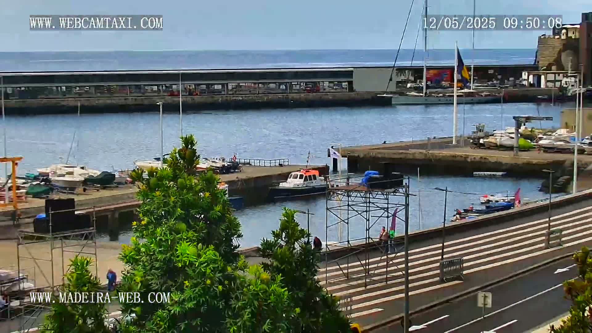 A harbor filled with boats on a partly cloudy day, with a small, orange pilotage boat in the foreground.