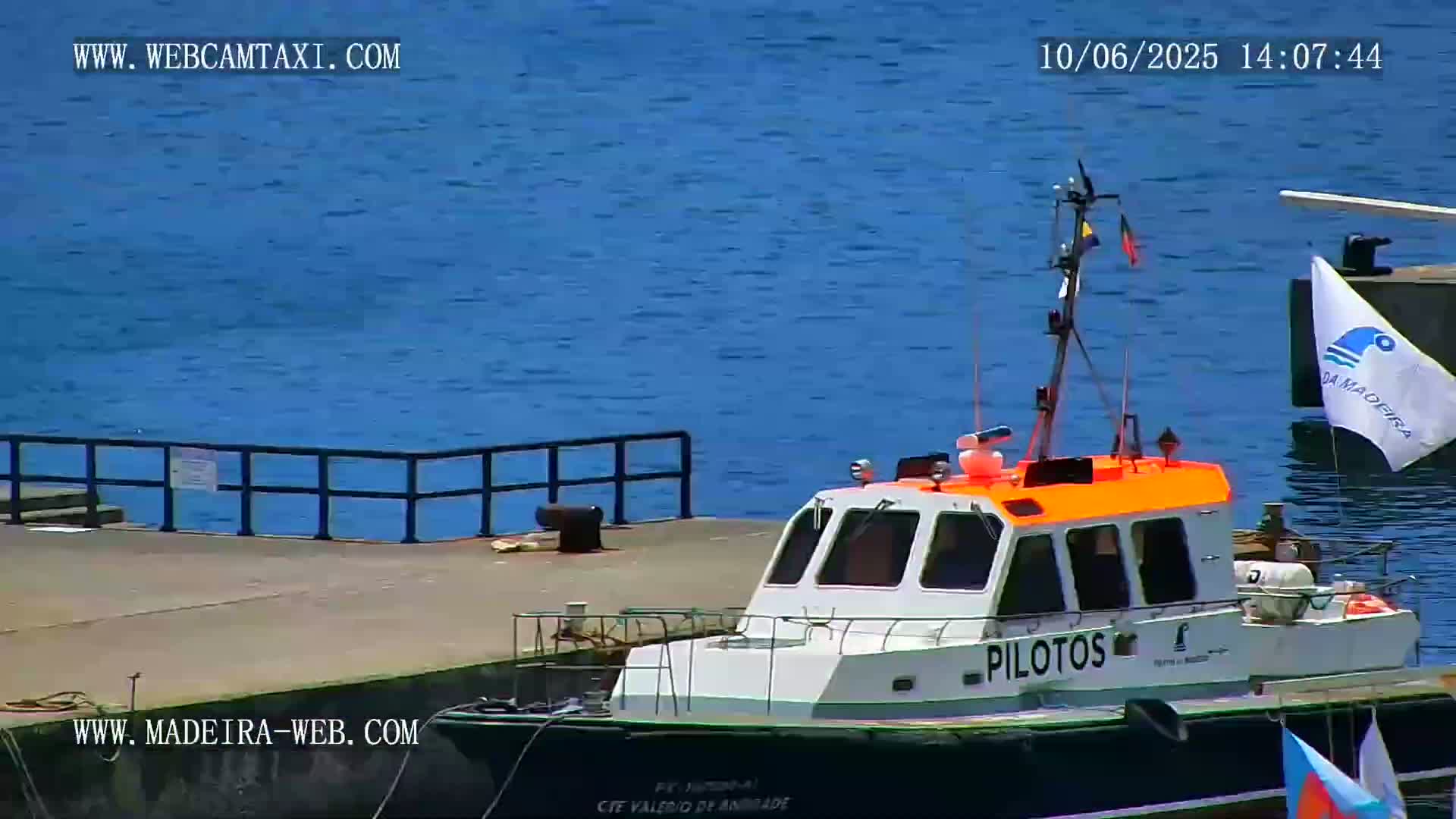 A white and orange pilot boat is docked at a pier next to calm, blue water.