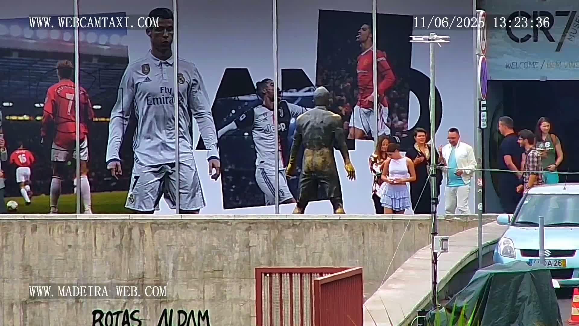 A large billboard depicting Cristiano Ronaldo in various soccer uniforms is displayed outdoors, with several people standing in front of it on a sunny day.