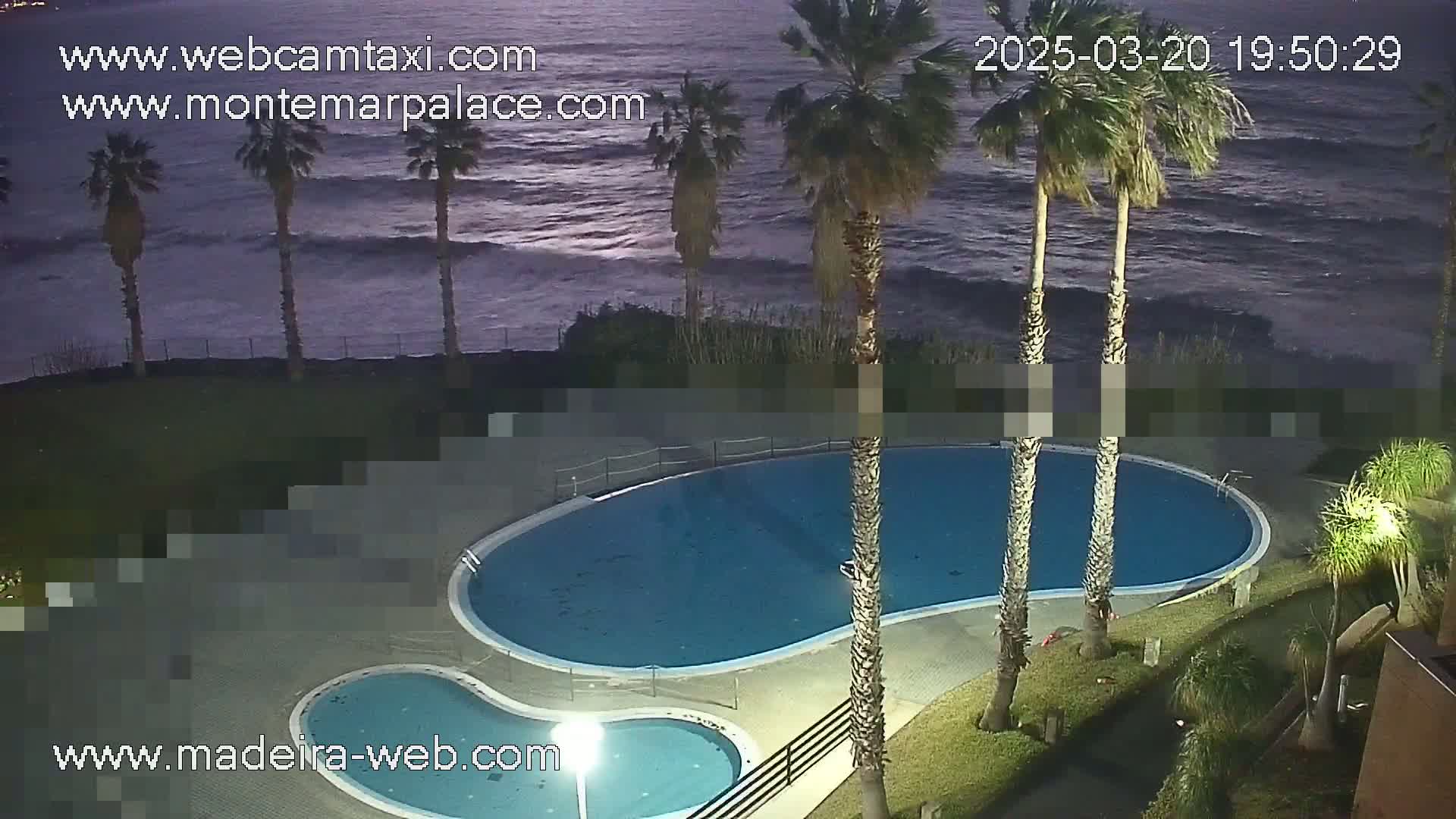 An outdoor swimming pool complex is situated beside a dark ocean under a twilight sky.