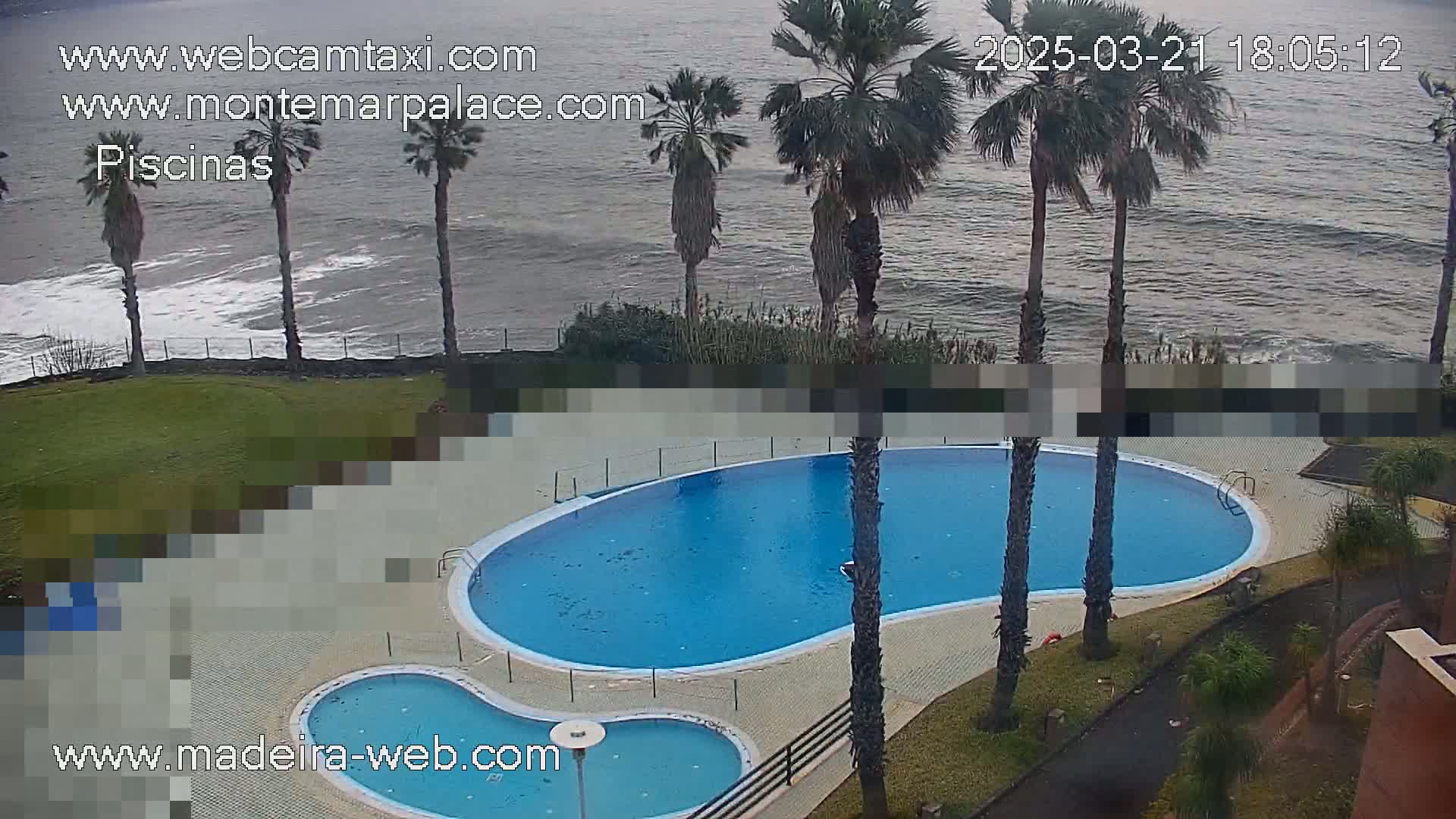 An outdoor kidney-shaped swimming pool and a smaller adjacent pool are situated next to a grassy area overlooking a choppy ocean under a cloudy sky.
