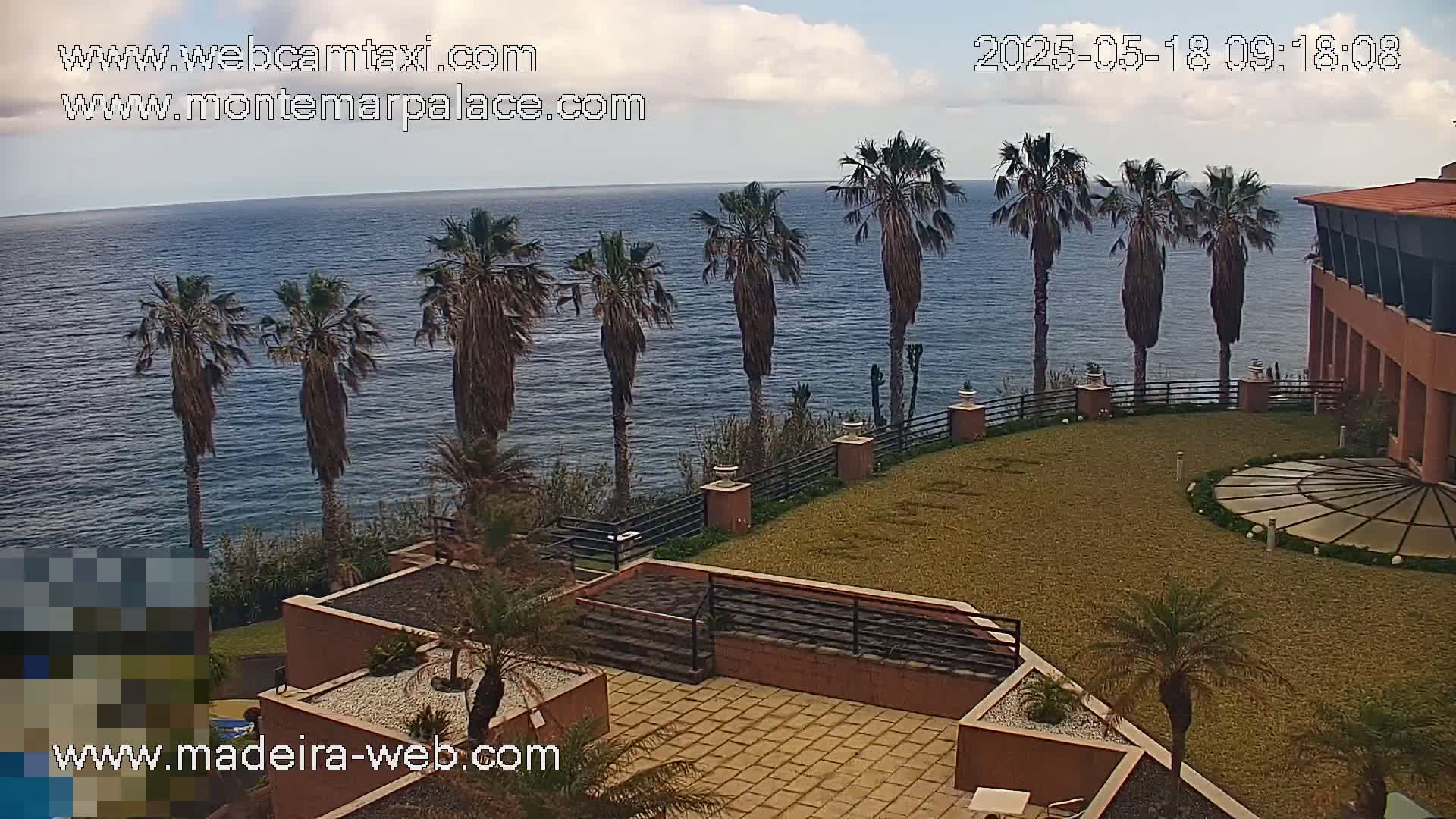 A partly cloudy day overlooking a calm ocean from a clifftop, featuring a resort with palm trees and manicured lawns.