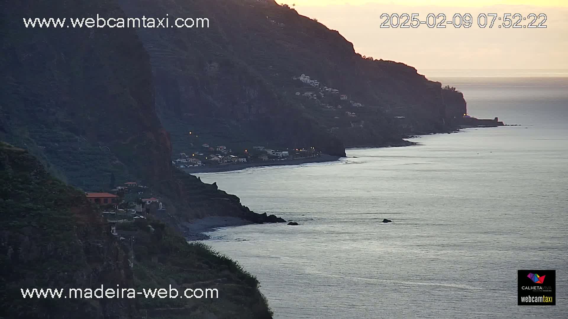 A calm ocean meets a dark, cliff-lined coast at sunrise.