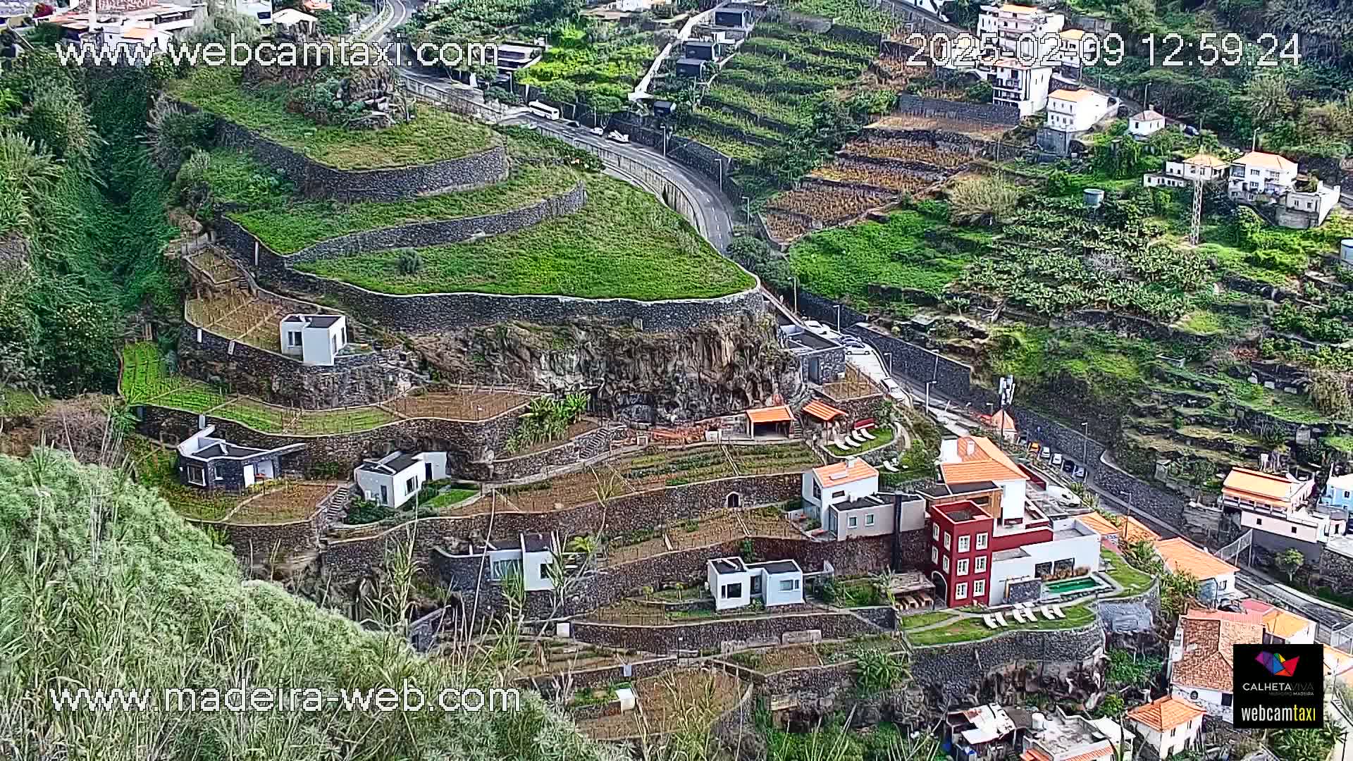 A high-angle view shows terraced farmland and buildings nestled into a hillside, with a road winding through the landscape.