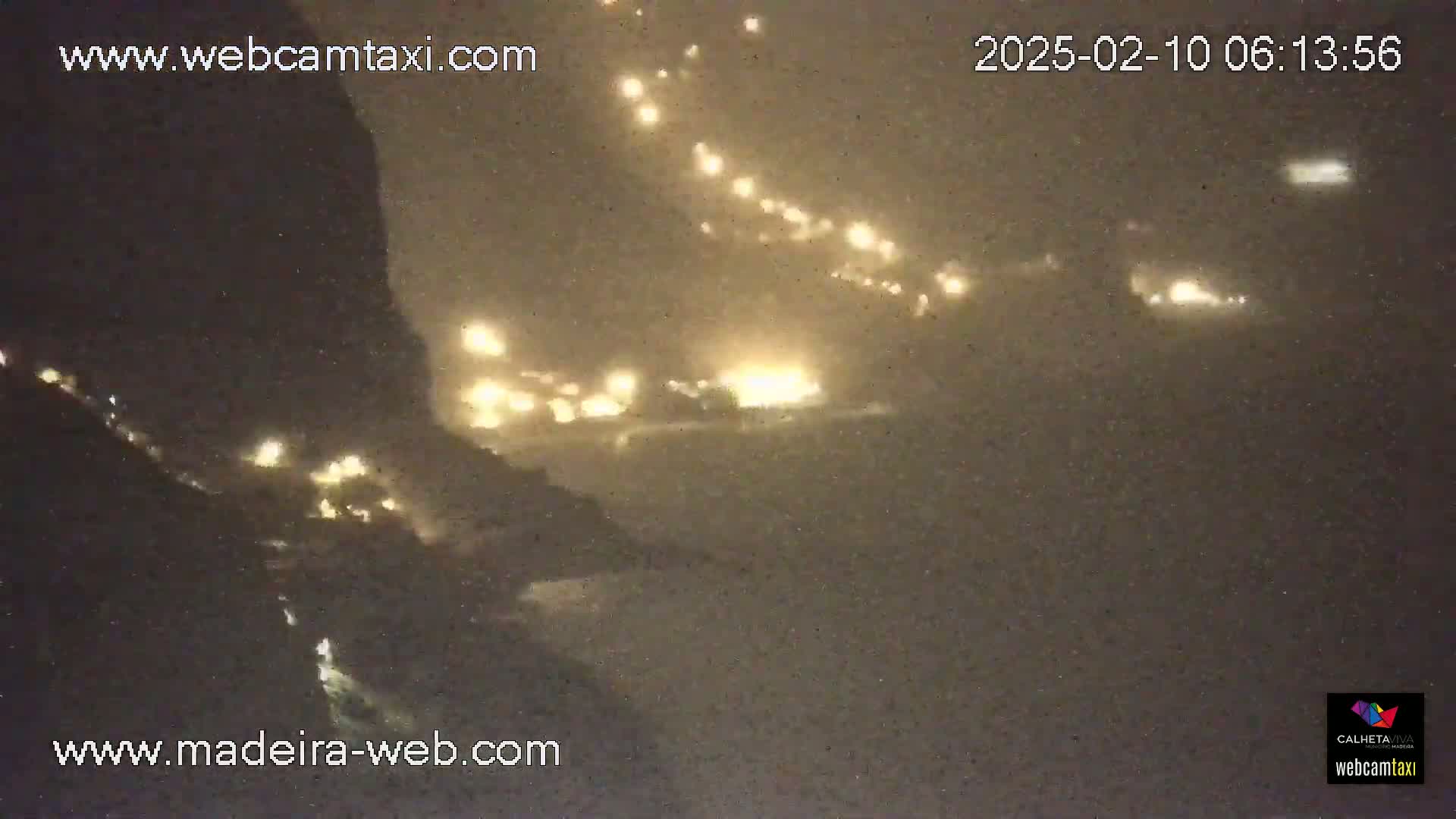 A nighttime view of a coastal area with numerous lights visible through a hazy or snowy atmosphere.