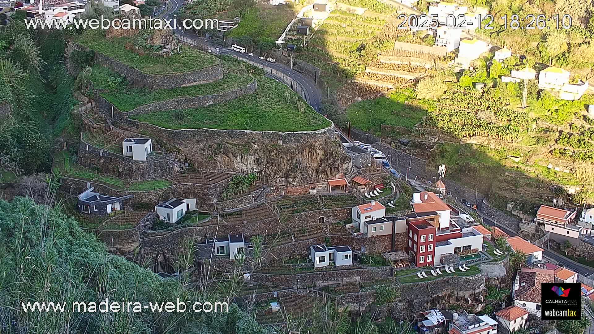 Terraced hillside farmlands with small buildings and a road wind down a steep cliffside in the late afternoon sun.