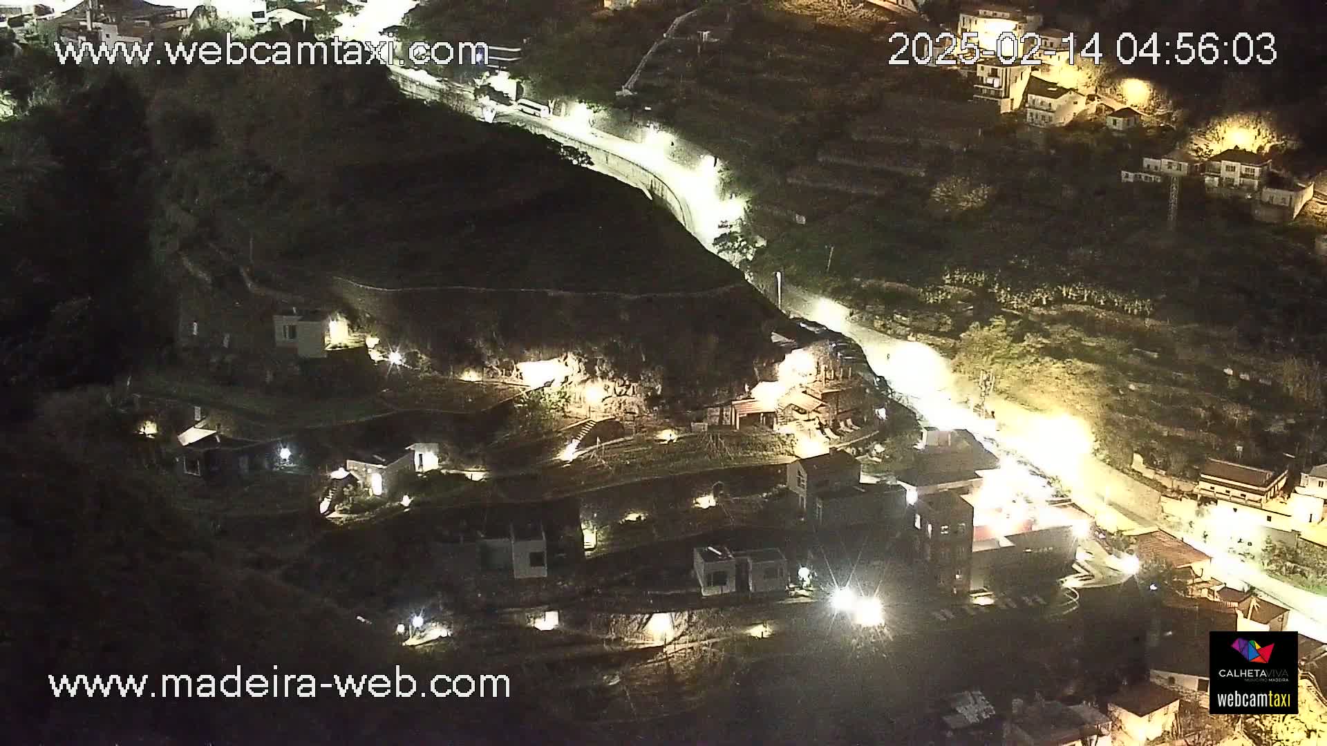 An aerial nighttime view of a hillside village with illuminated buildings and a winding road.