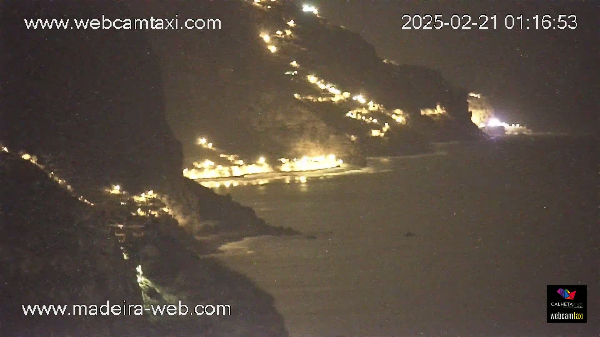 A nighttime coastal scene shows a dark cliffside with illuminated buildings and a dark ocean.