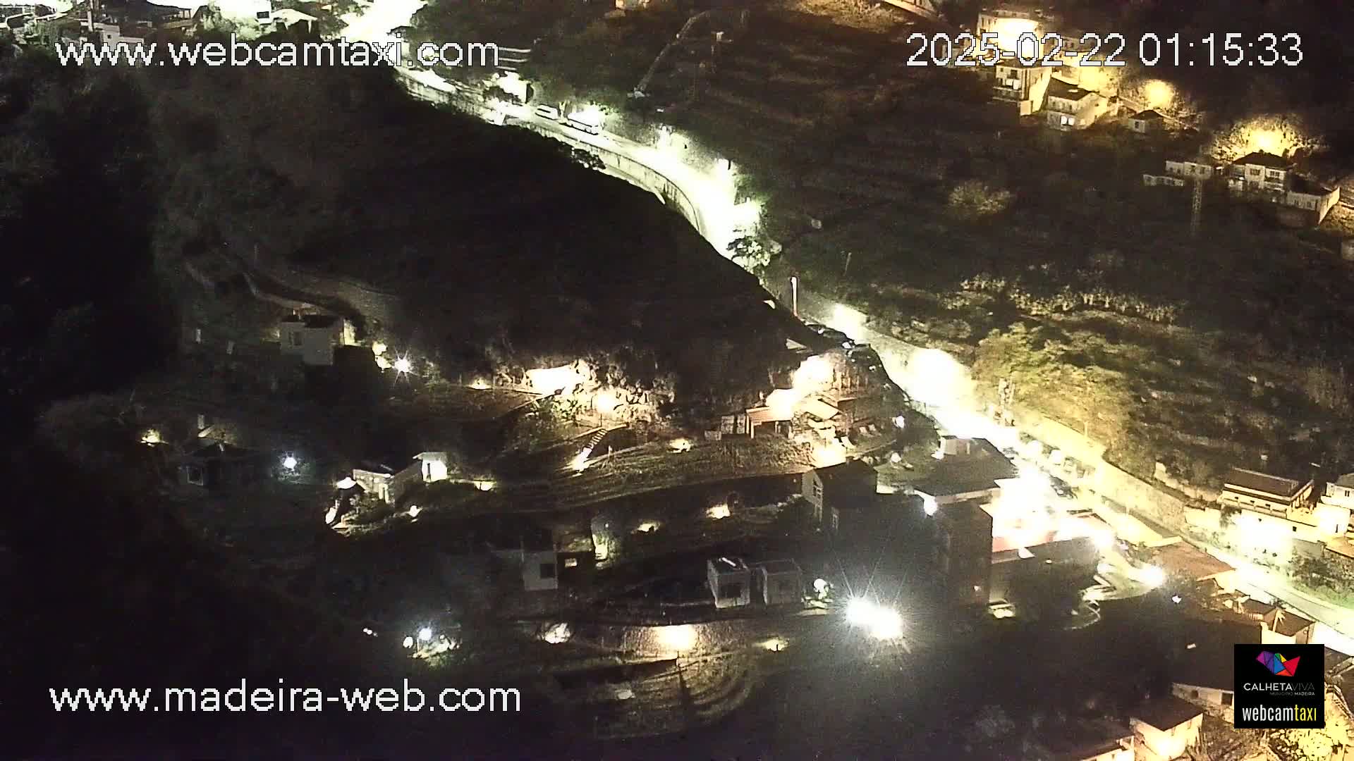 An aerial nighttime view of a hillside town with winding roads and sparsely lit buildings.