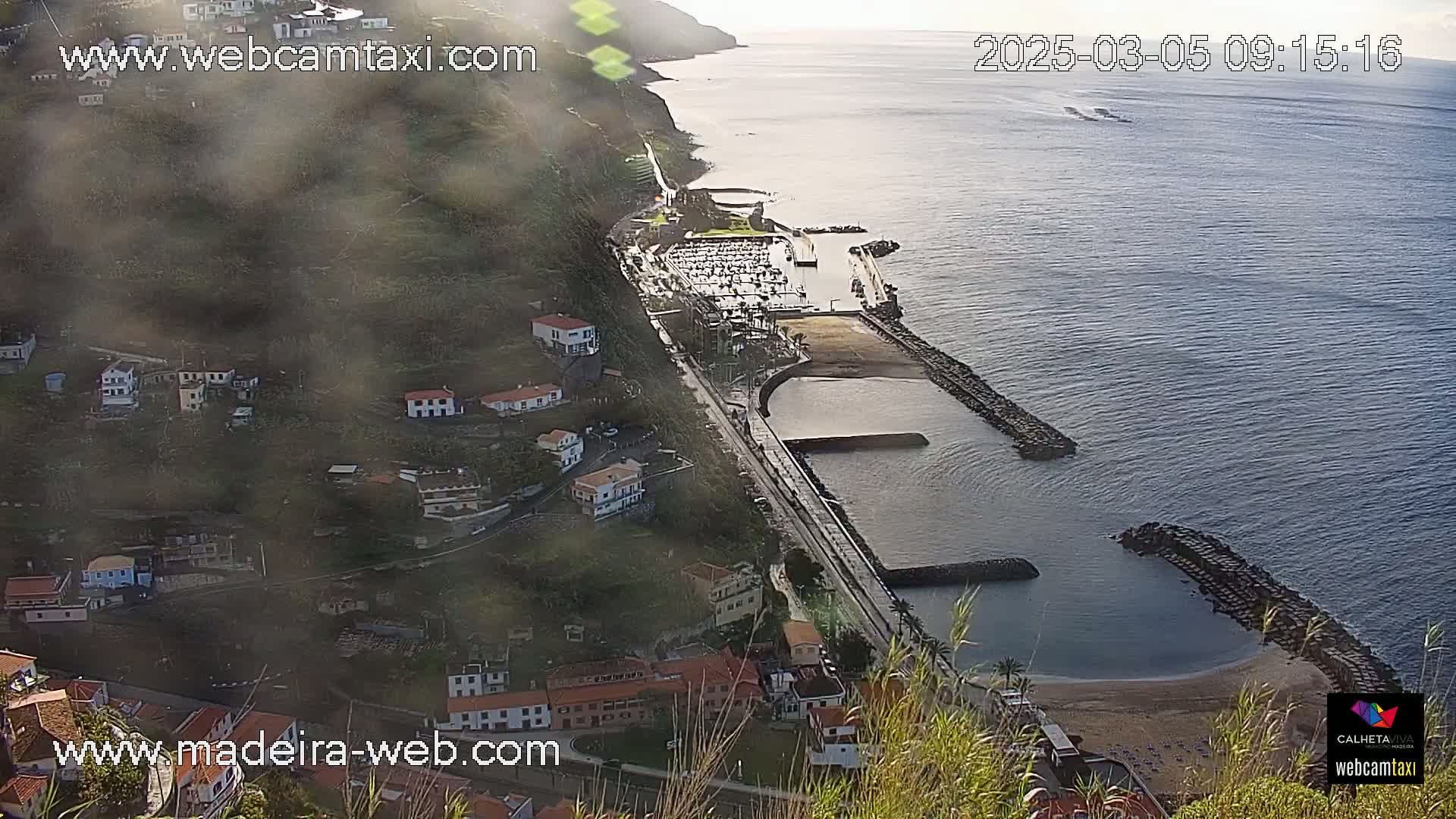 A coastal town with a marina nestled on a hillside overlooking a calm ocean, partially obscured by haze.
