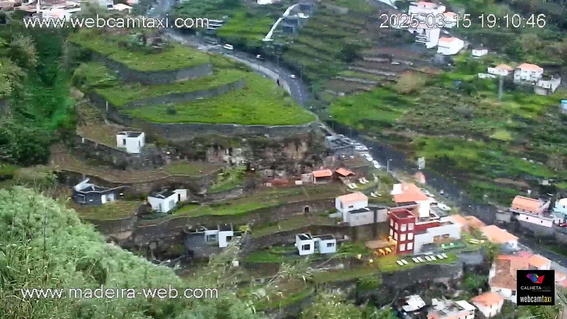 A rain-swept hillside village clings to terraced farmland, a road winding through the scene.